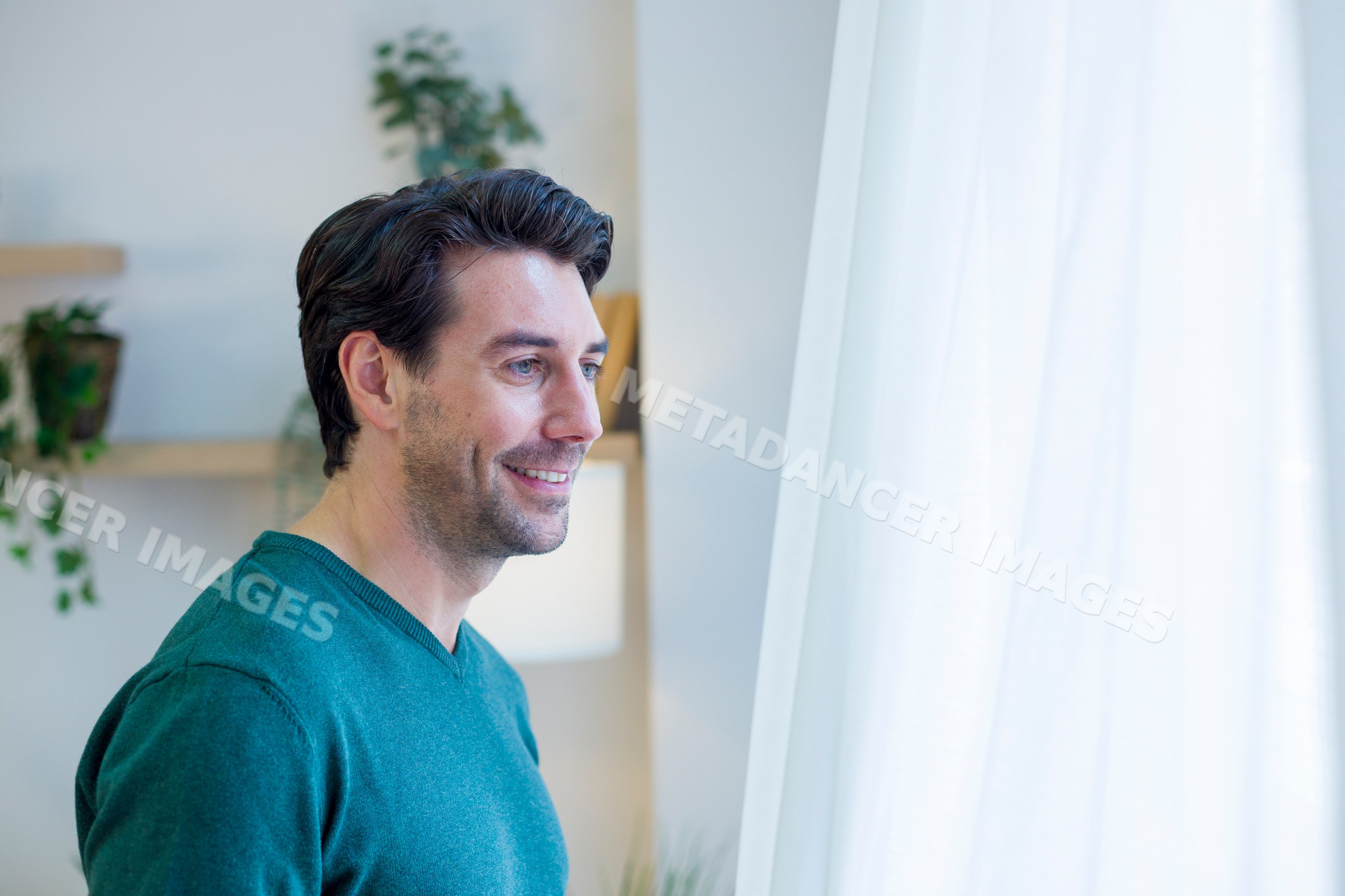 White man smiling and looking out window inside home