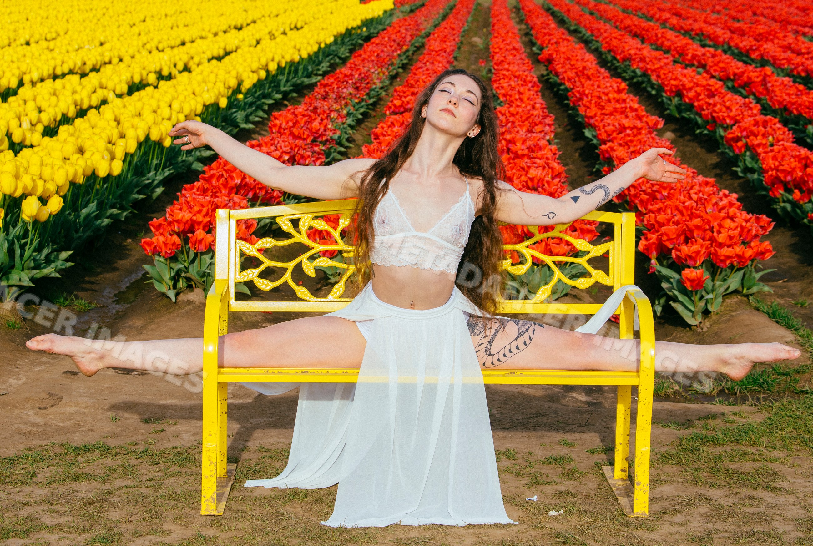 White woman doing split stretch on yellow bench in tulip field