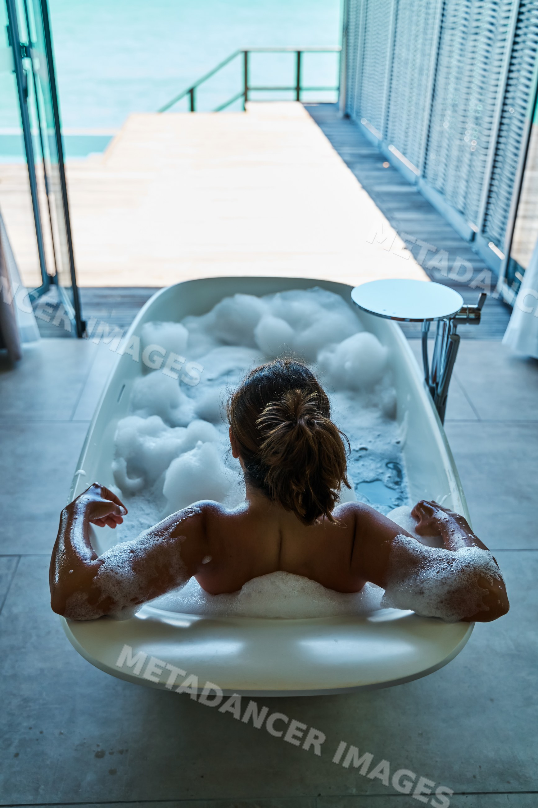 A white woman relaxes in a bubble bath with ocean view