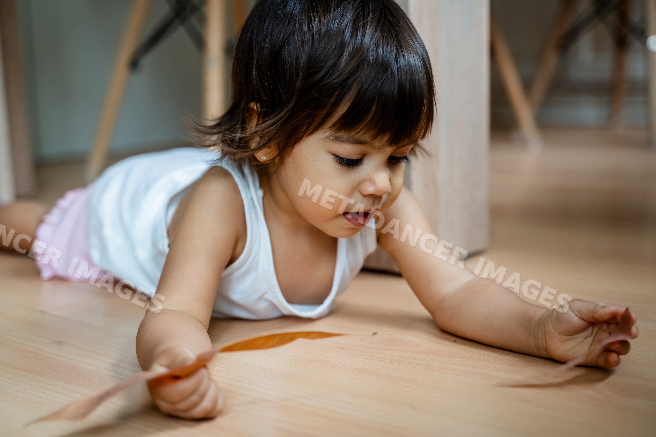 Toddler white girl playing with leaf on indoor wooden floor in a home