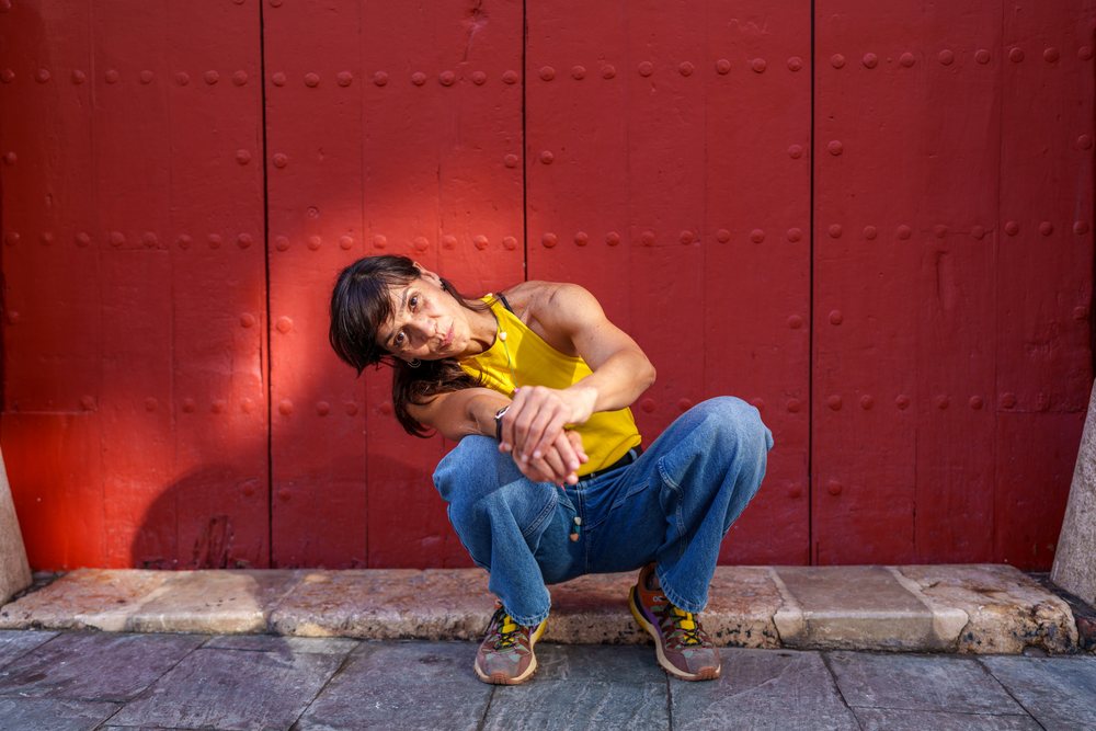 Hispanic woman squatting by red door on street in Málaga Spain
