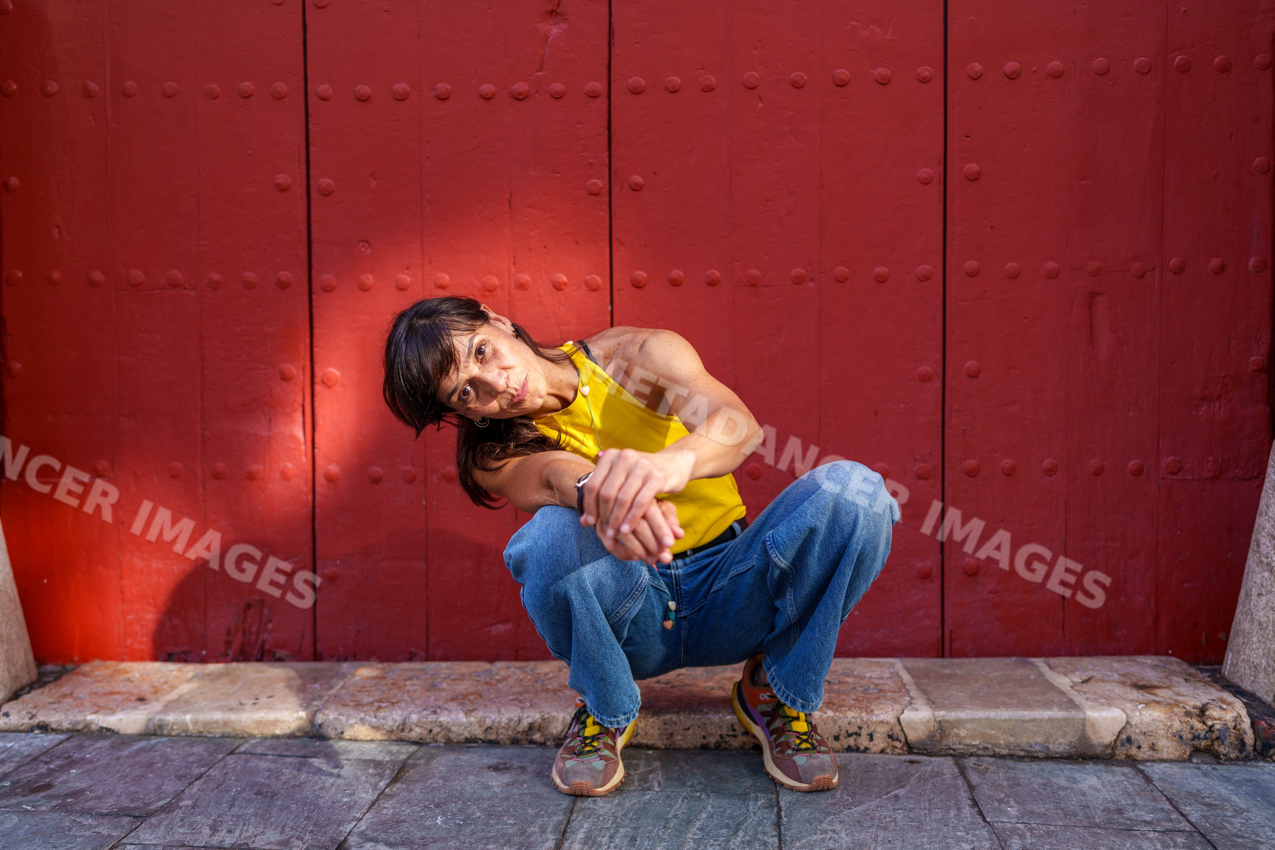 Hispanic woman squatting by red door on street in Málaga Spain