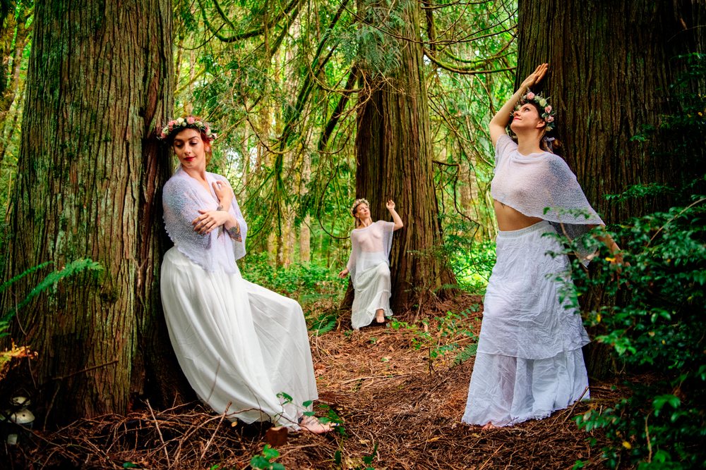 White women posing gracefully in a green forest with floral crowns