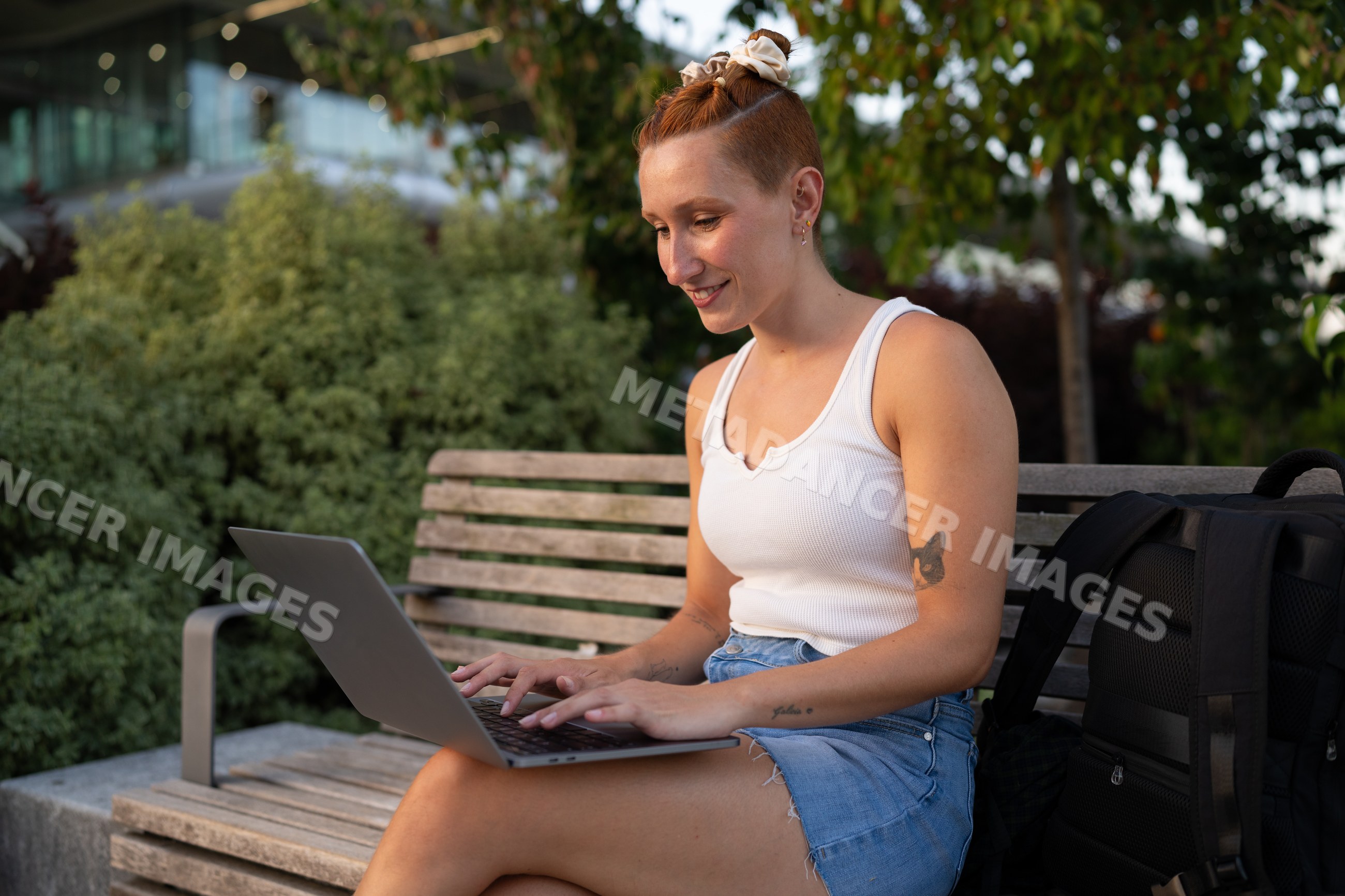 Young white woman typing on laptop while sitting outdoors in a park