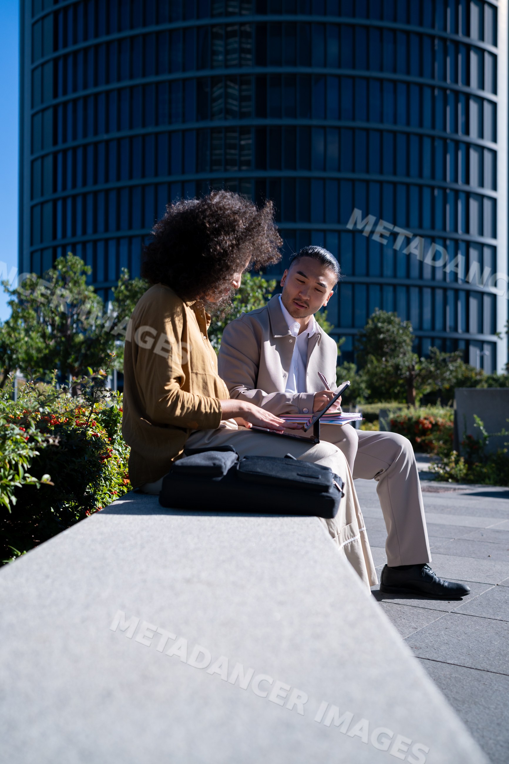 Two men using tablet and notebook near modern building