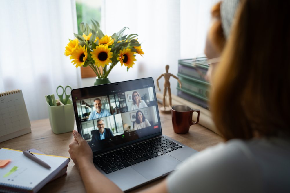 A white woman telecommutes with colleagues on a video call