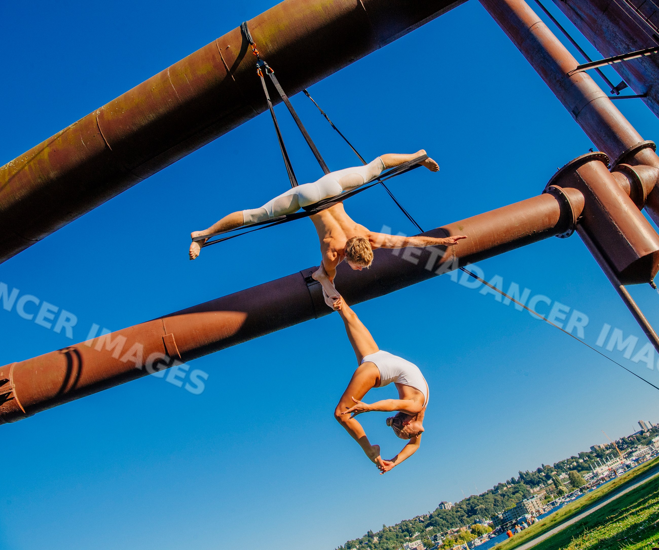 Aerial acrobats performing yoga on steel structure outdoors in a park