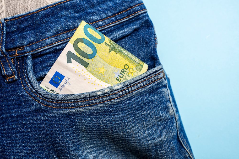 100 euro banknote in blue denim jeans pocket on blue background