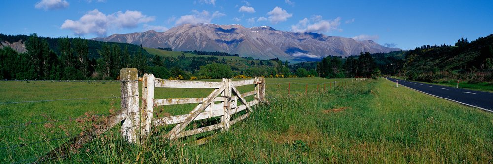 Wooden gate in grassy field next to road with mountain view