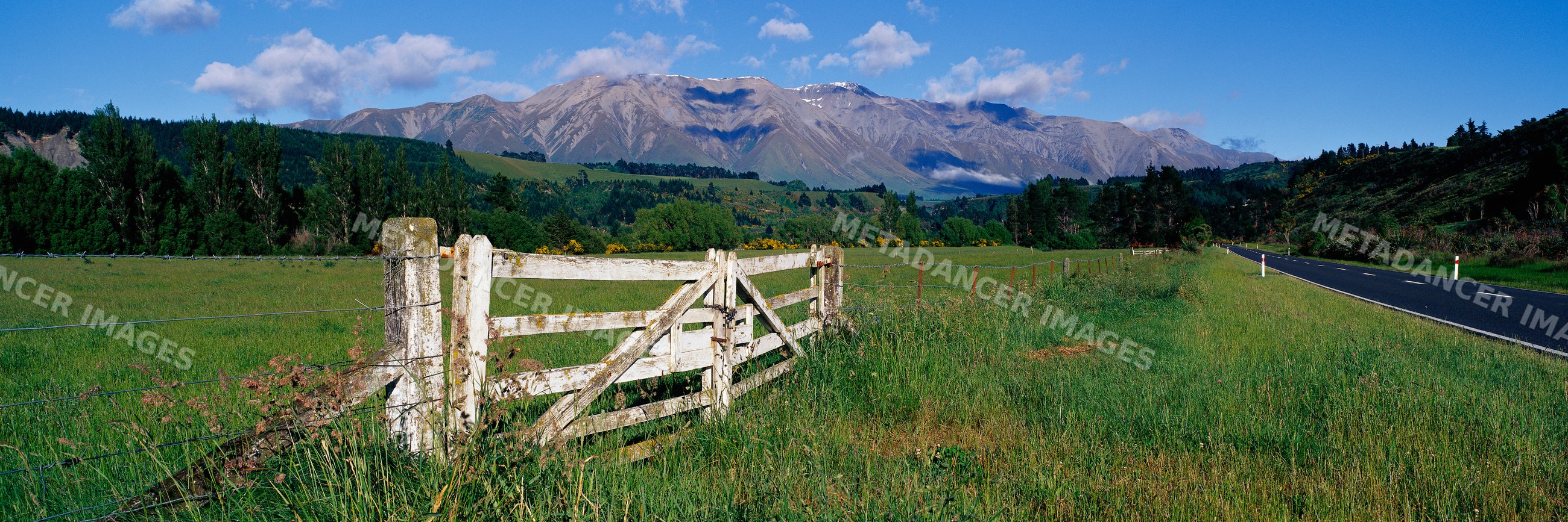 Wooden gate in grassy field next to road with mountain view