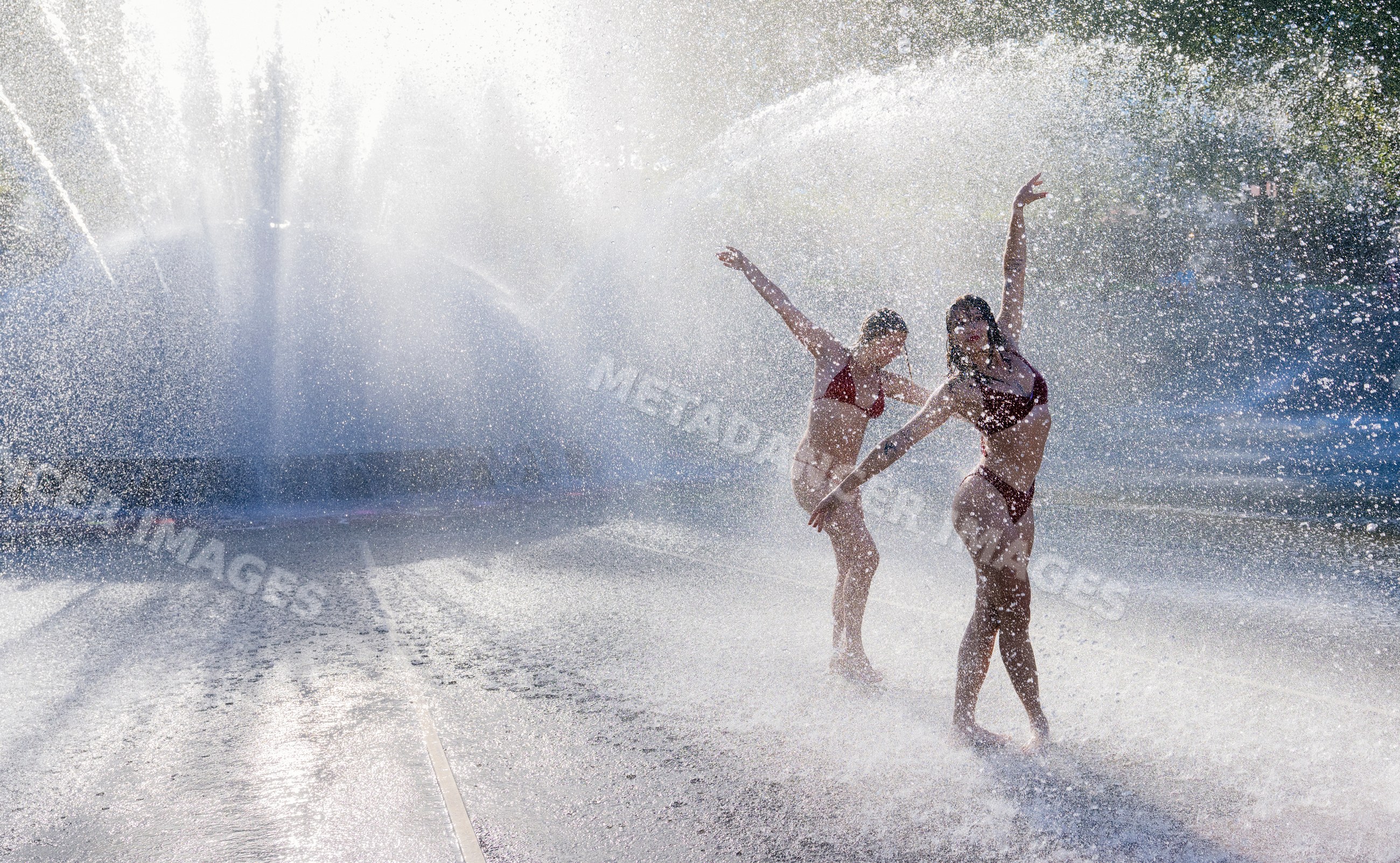 Two white women dancing in a water fountain spray outdoors