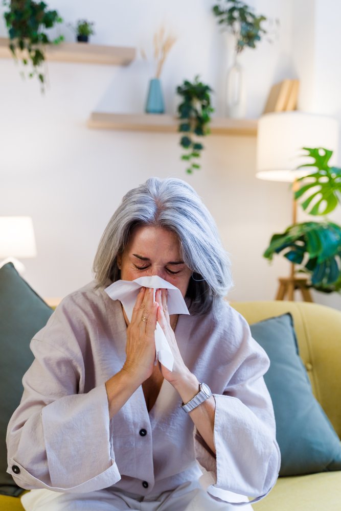 Older white woman sneezing on sofa in living room