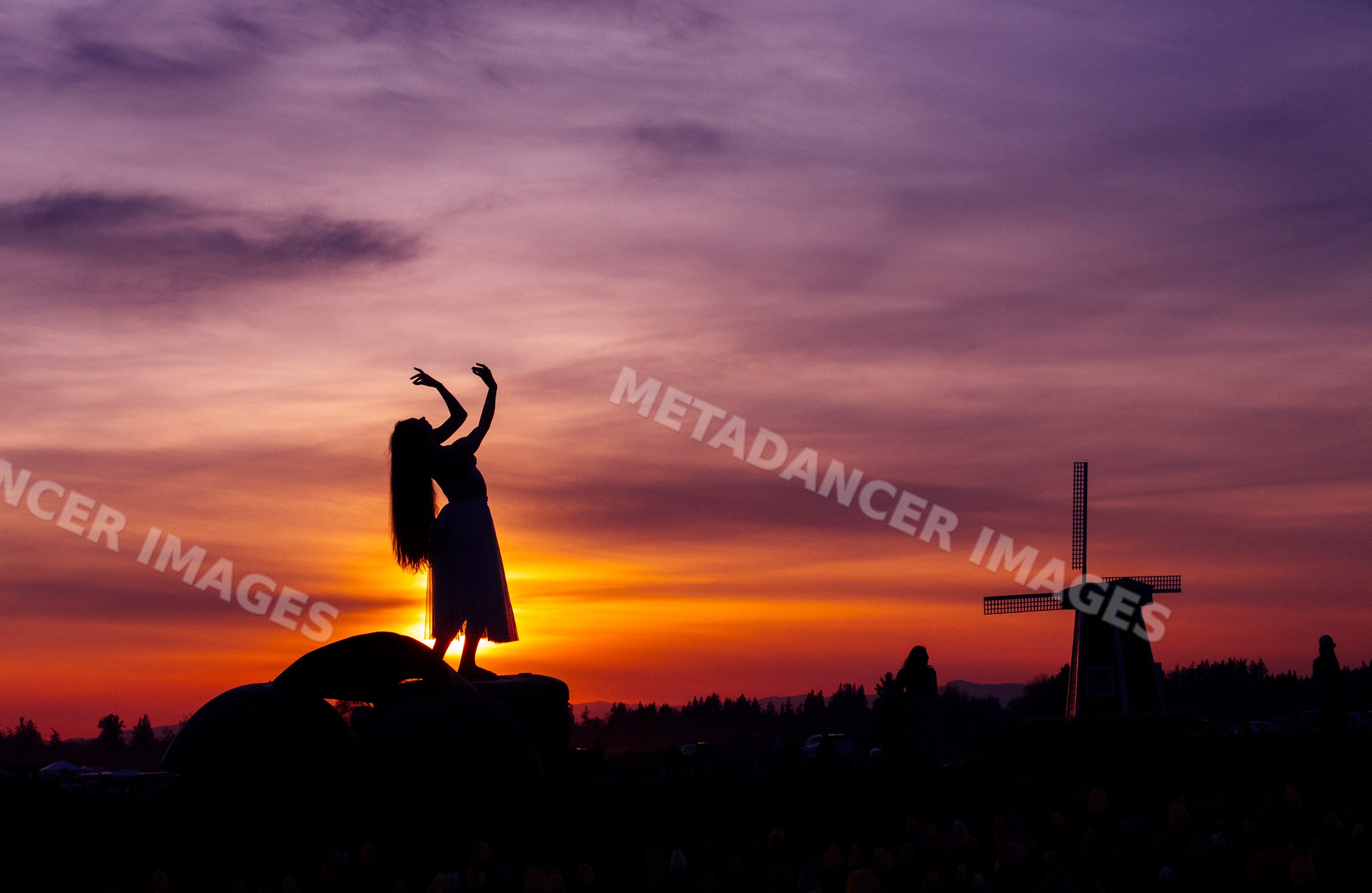 Silhouette of white woman dancing by windmill at sunset in USA