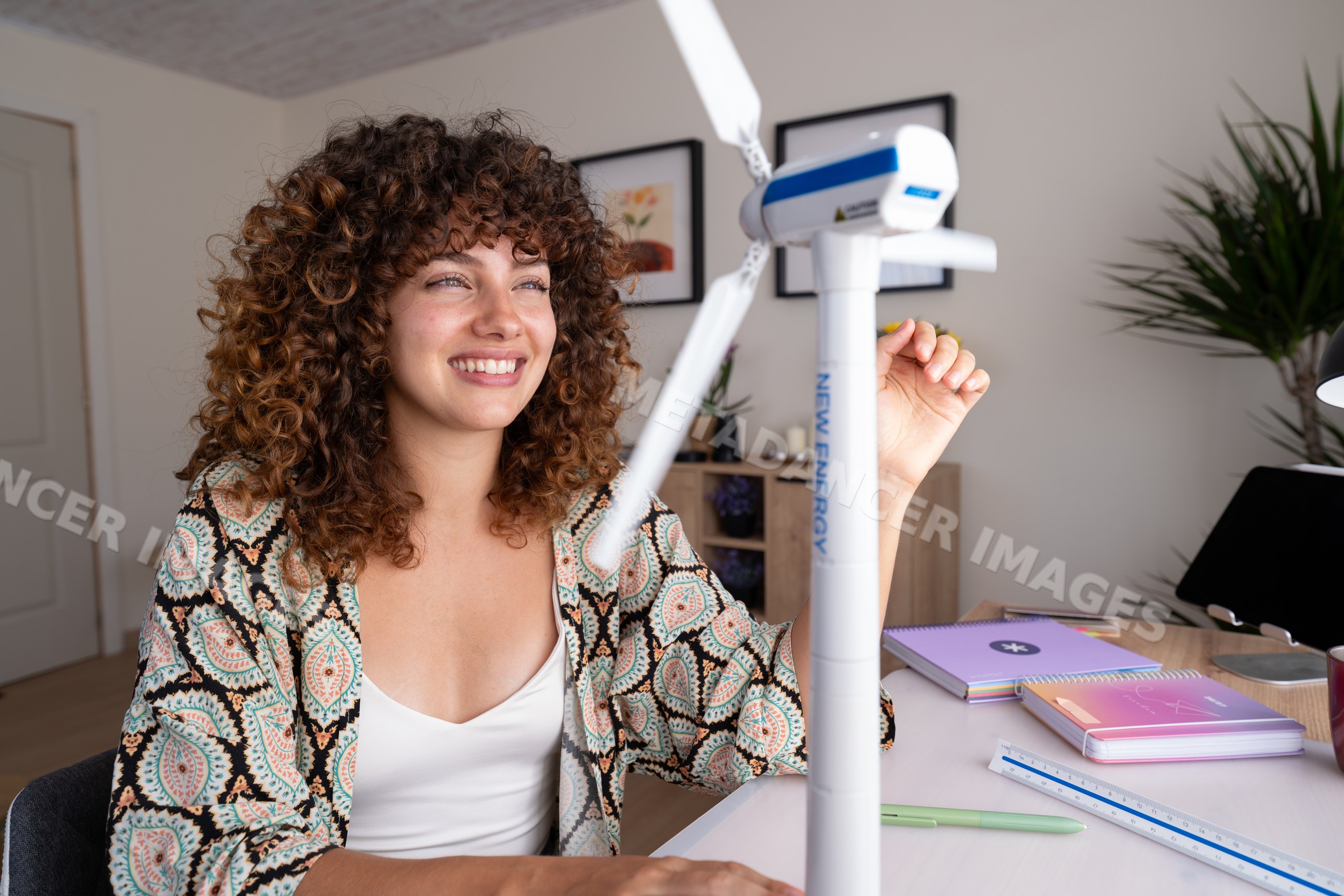 White girl examining small model wind turbine at home desk in Spain