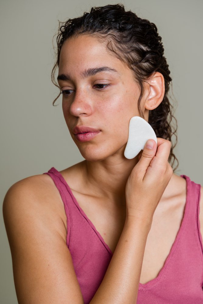 Hispanic woman using a gua sha tool for facial massage indoors