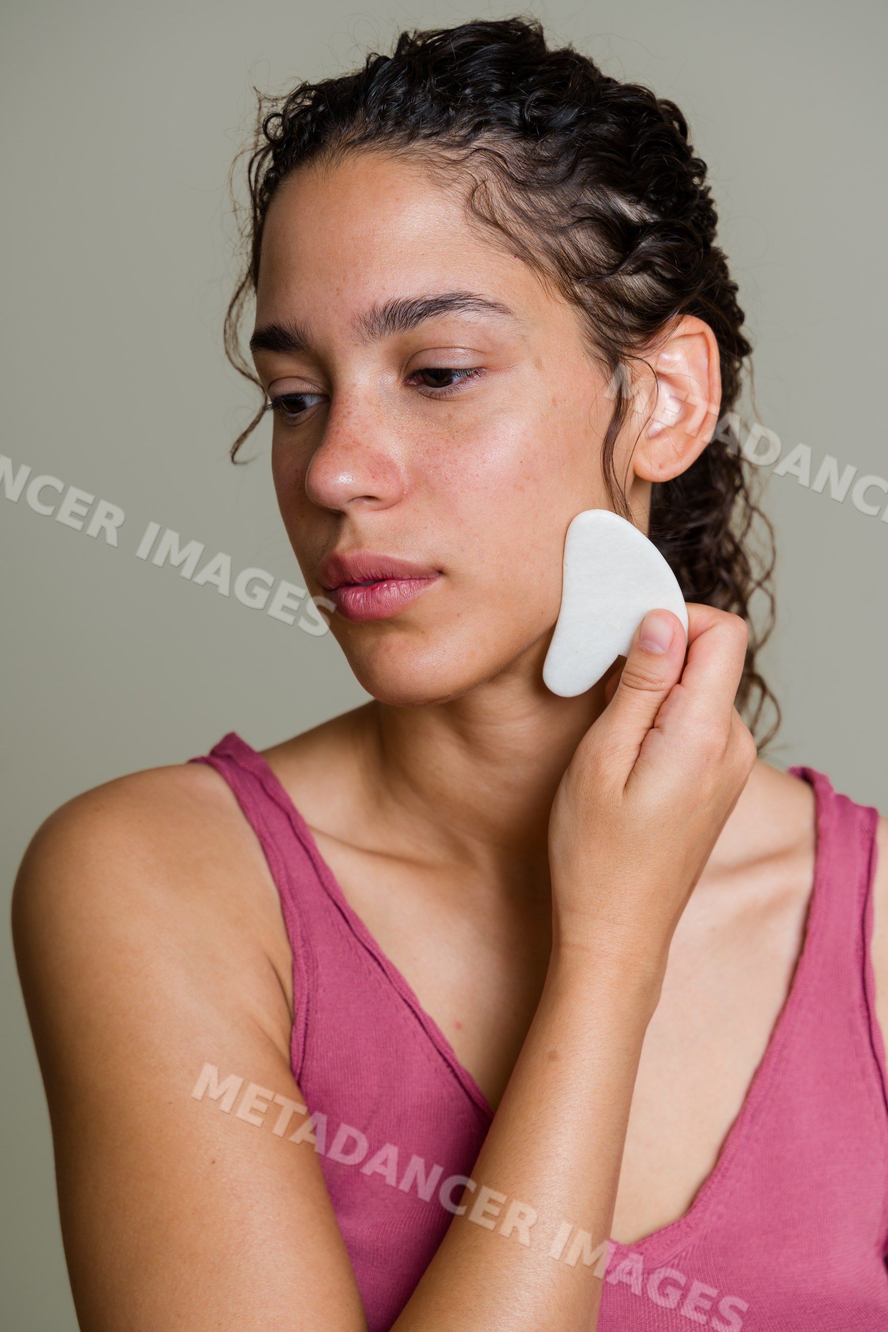 Hispanic woman using a gua sha tool for facial massage indoors