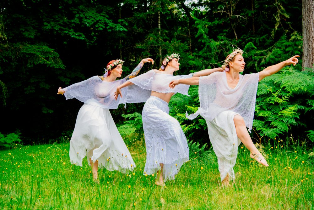 Women dancing barefoot in white skirts in forest clearing