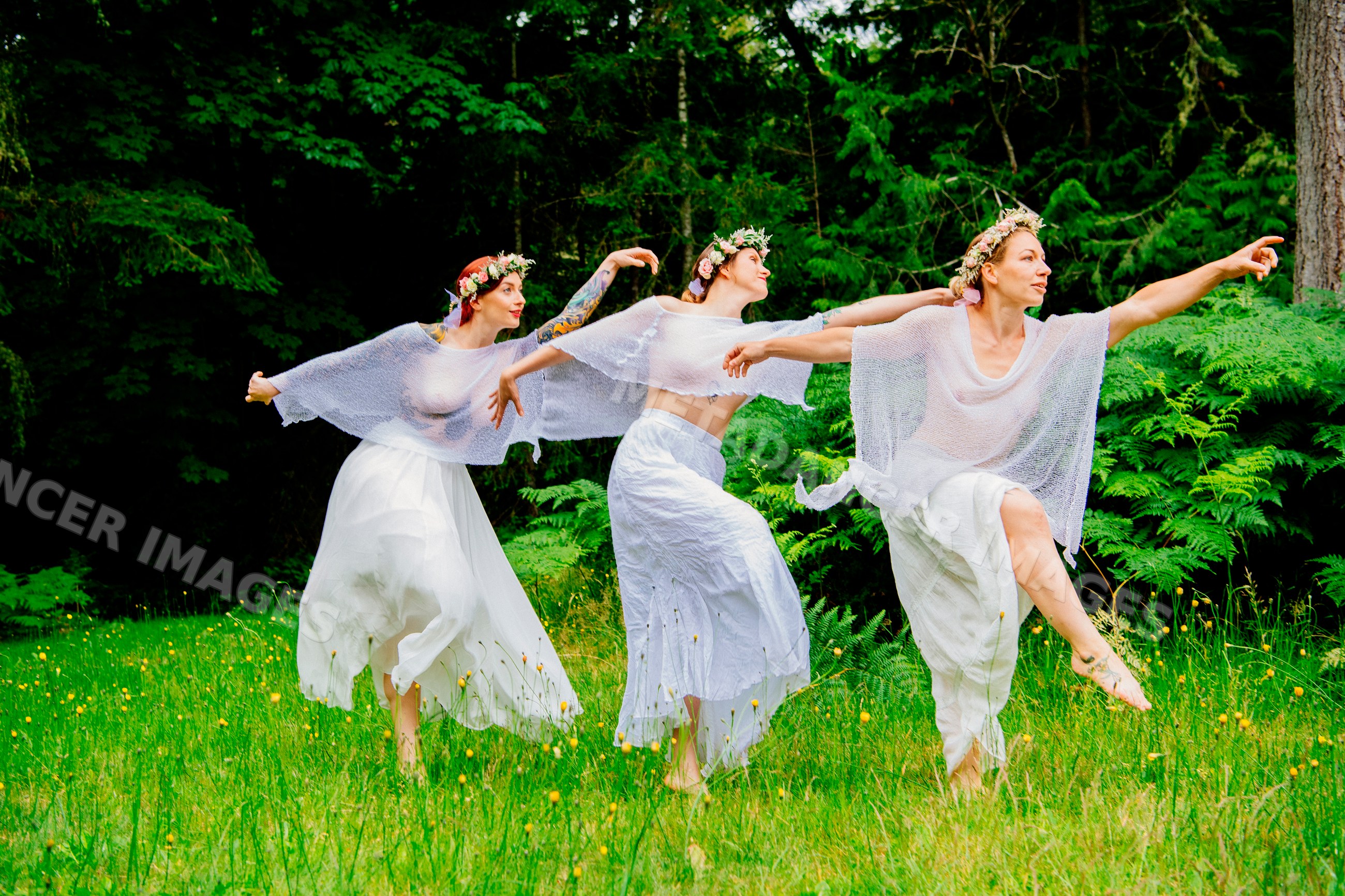 Women dancing barefoot in white skirts in forest clearing