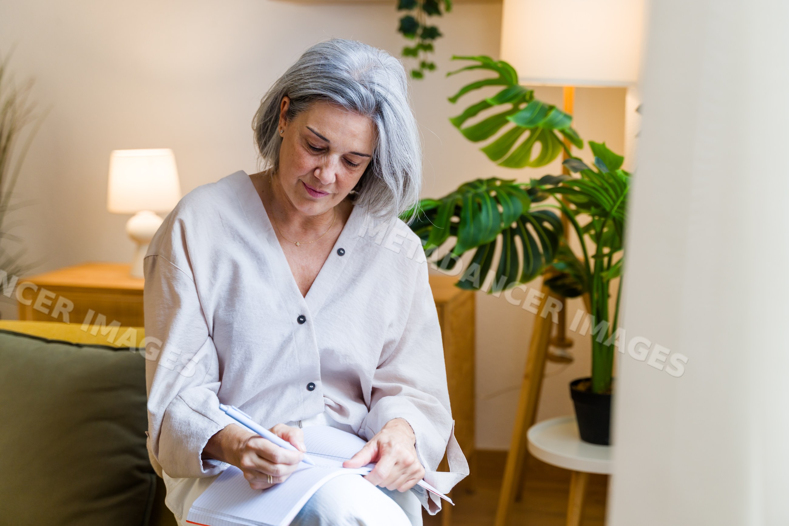 White woman writing in notebook in cozy home setting with indoor