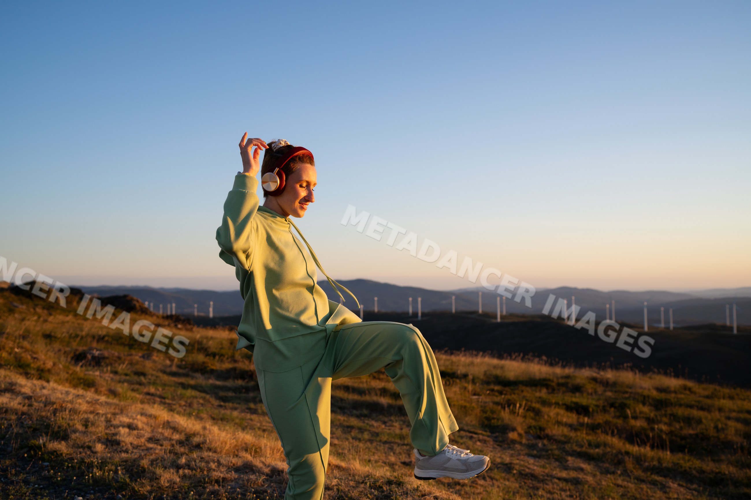A white woman dances to music outdoors at sunset in Galicia, Spain