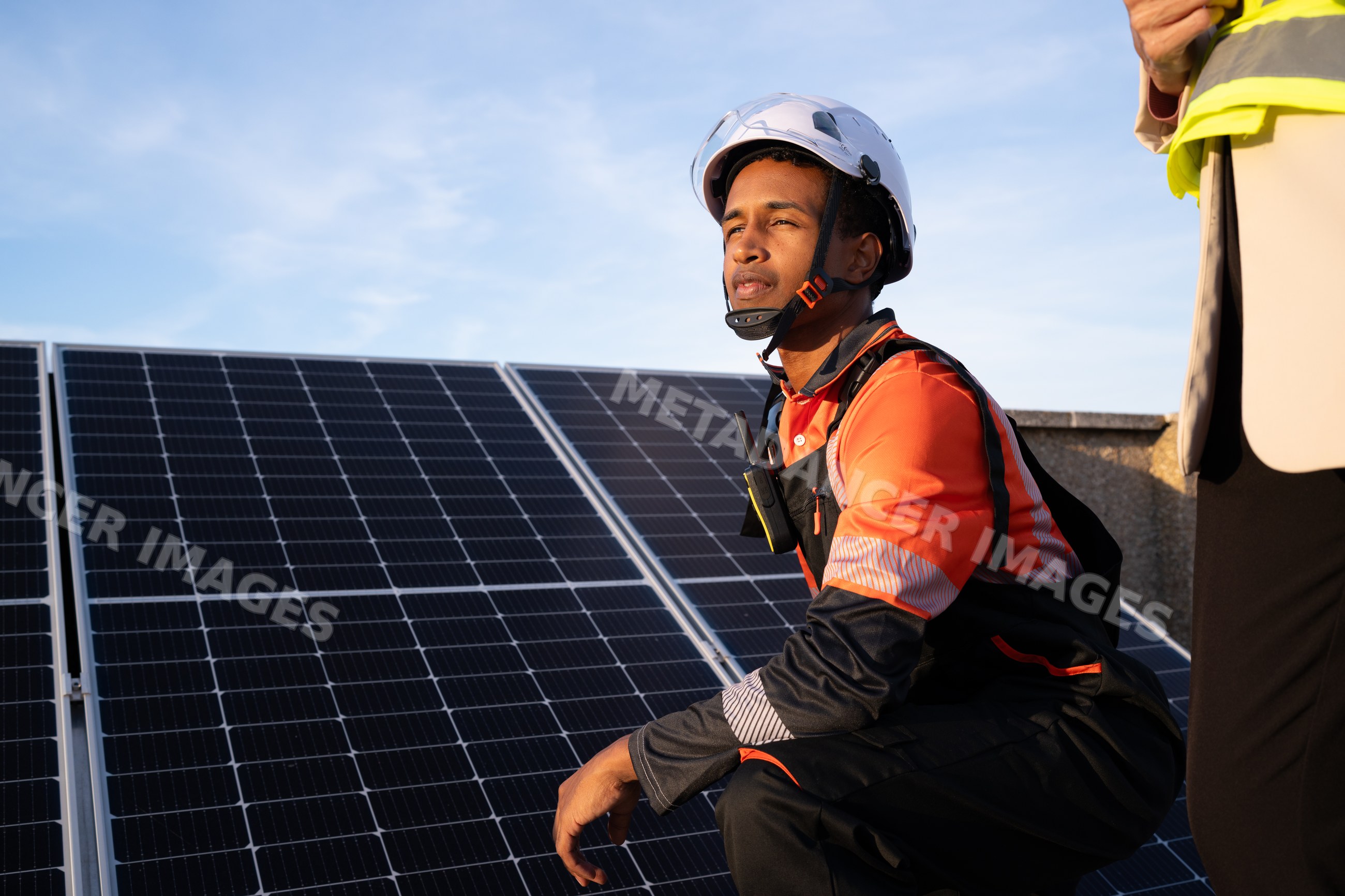 White worker crouching beside solar panel installation on rooftop