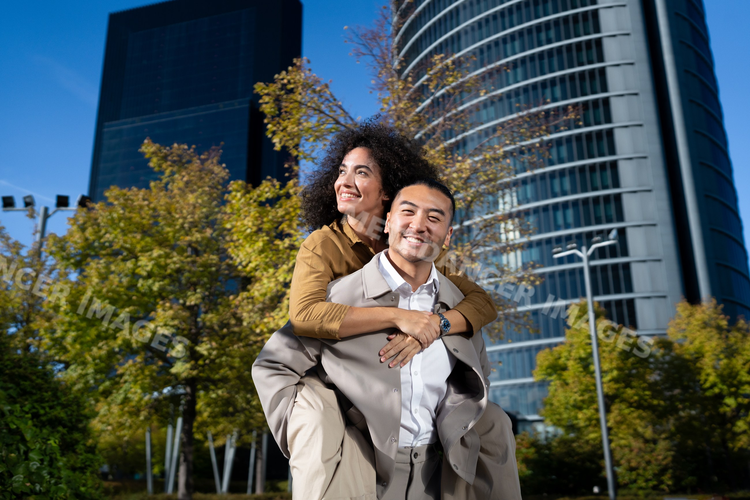 Couple enjoying a piggyback ride in urban park with modern buildings