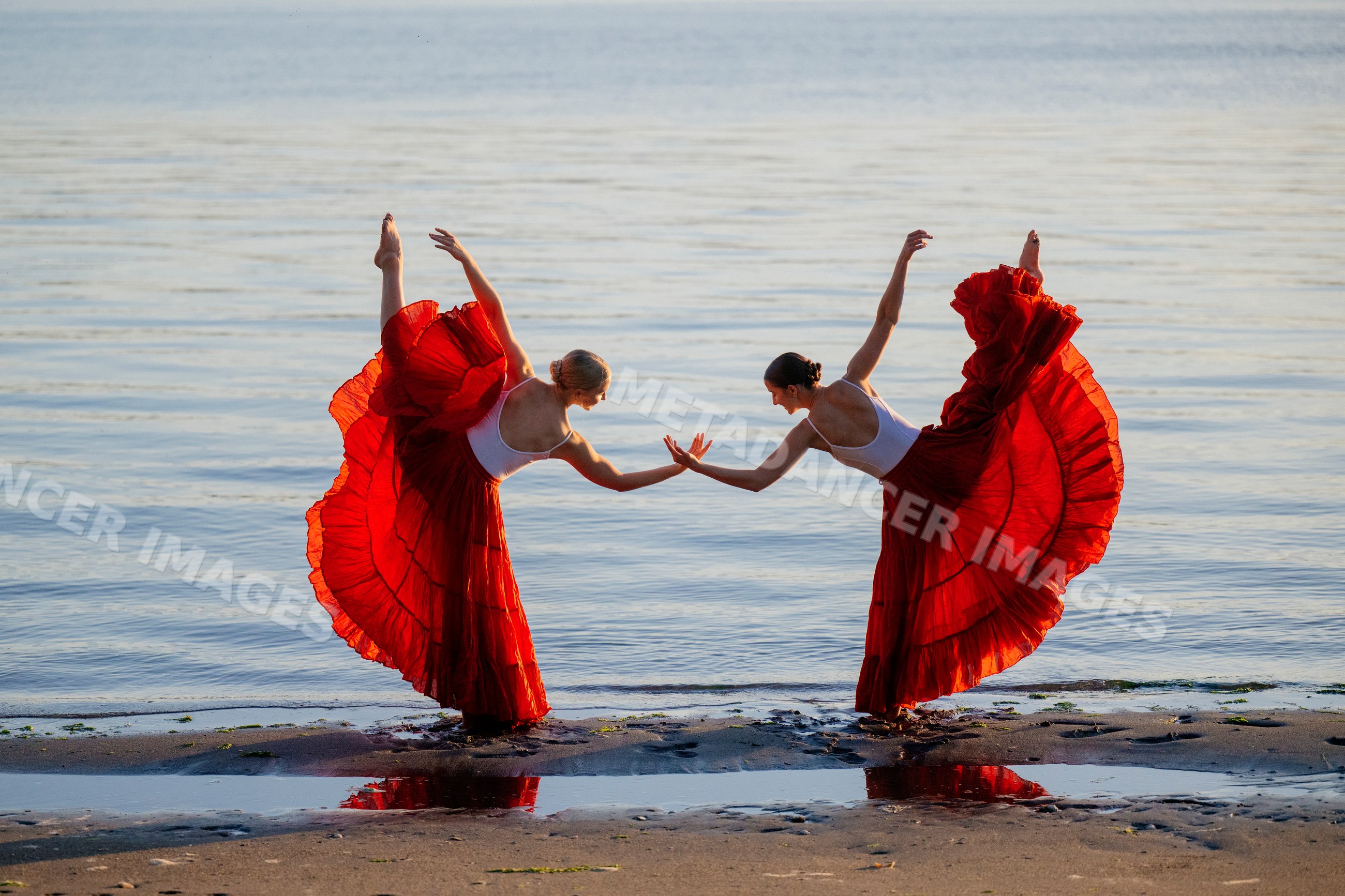 Two white women practicing partner acrobatics yoga on a beach