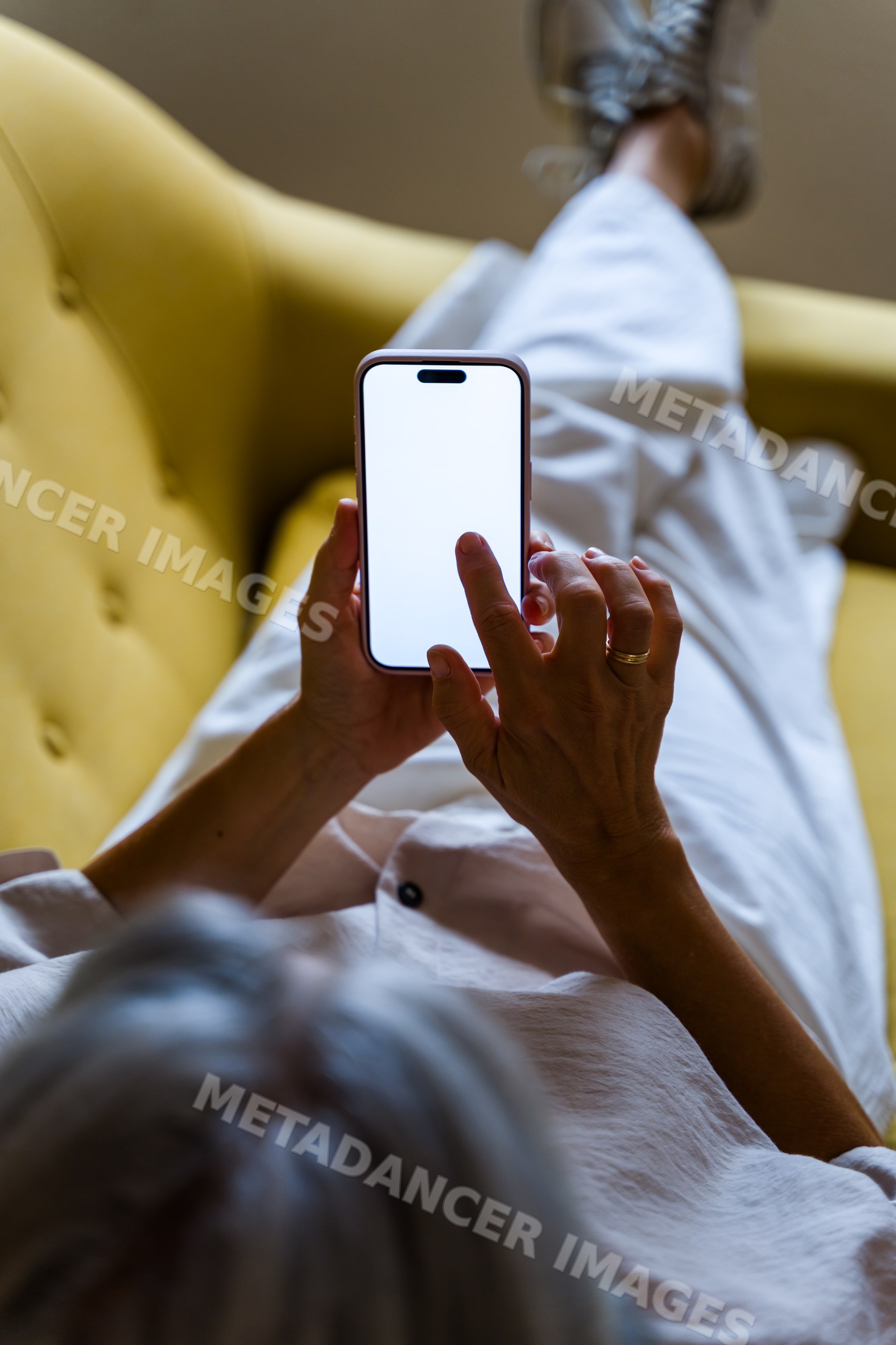 White man reclining on yellow couch using smartphone indoors