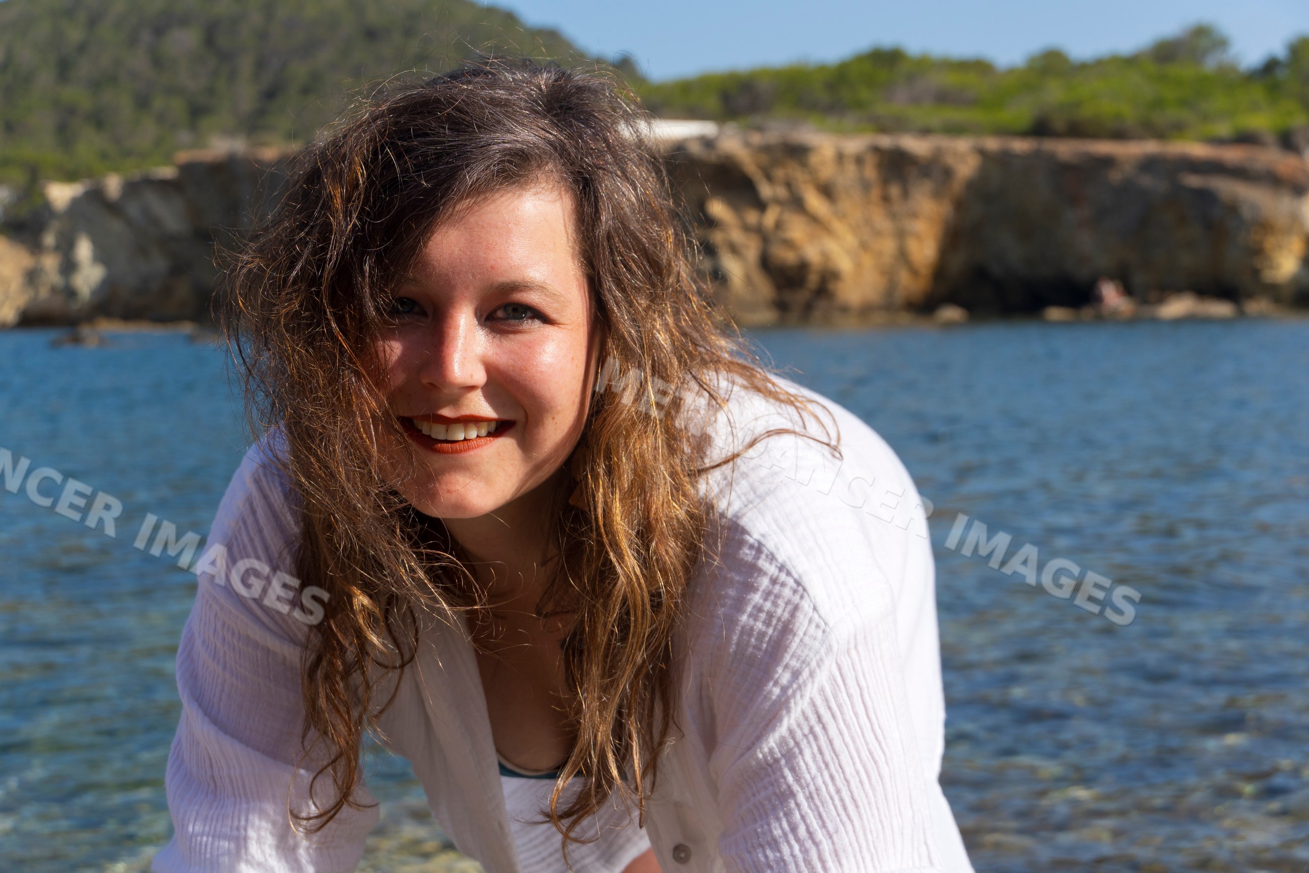 White woman smiling near water at rocky coastal shore in Ibiza, Spain
