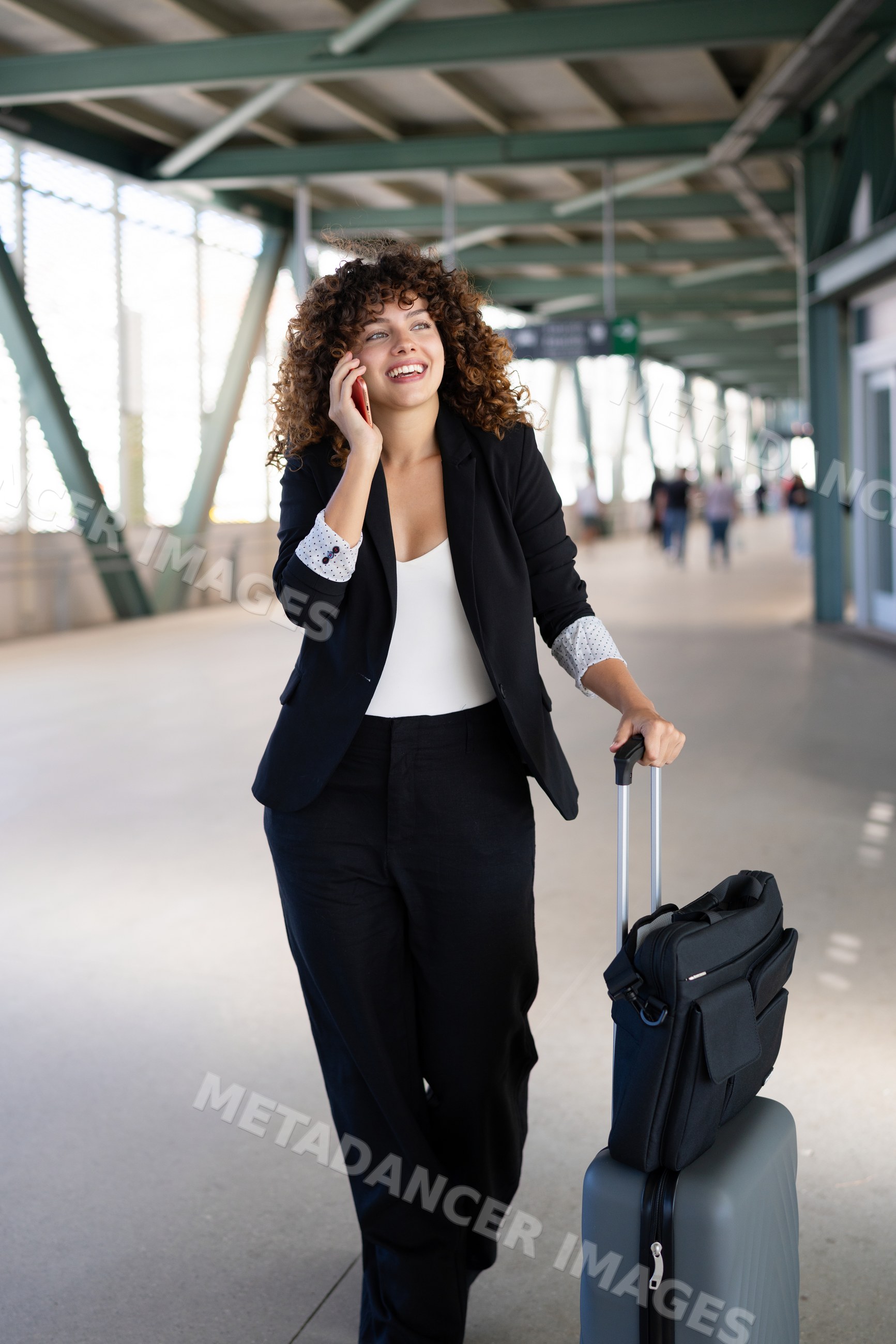 White woman walking through airport corridor with luggage and phone