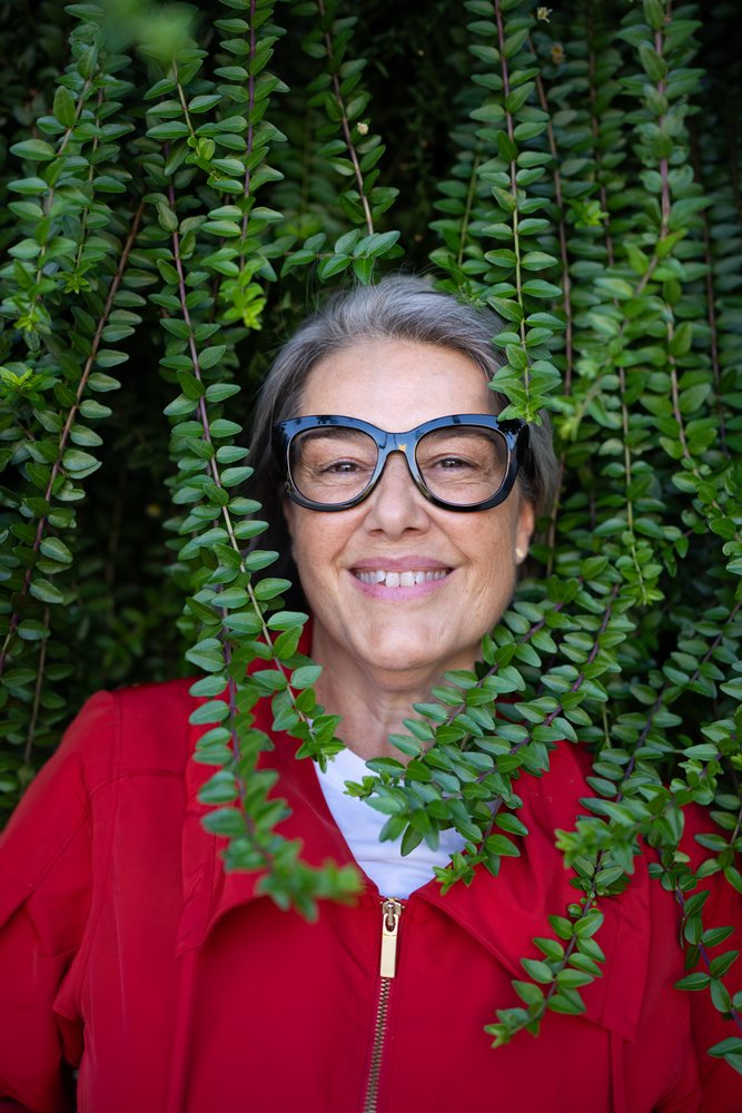 Smiling middle-aged white woman wearing glasses outdoors among green