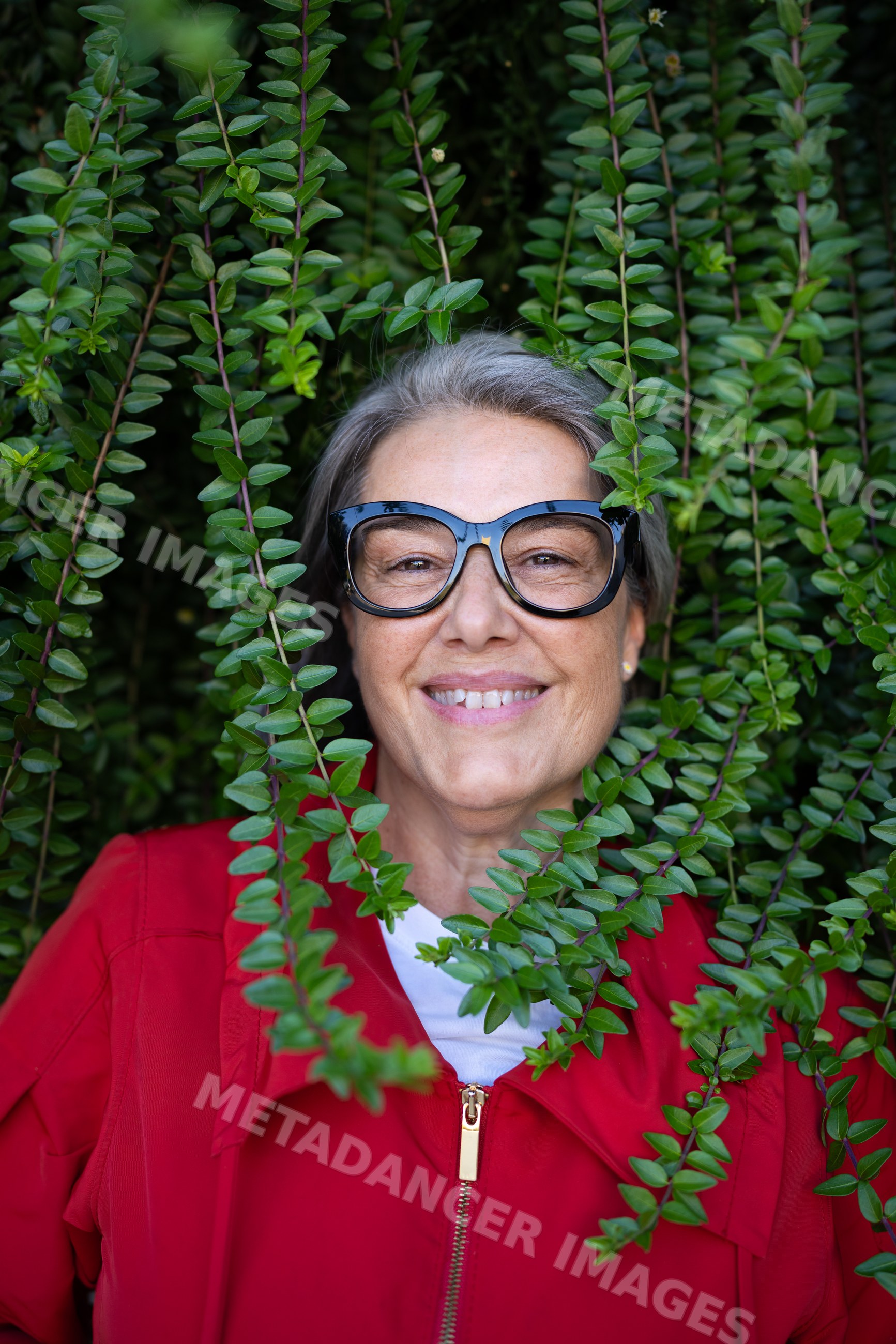 Smiling middle-aged white woman wearing glasses outdoors among green