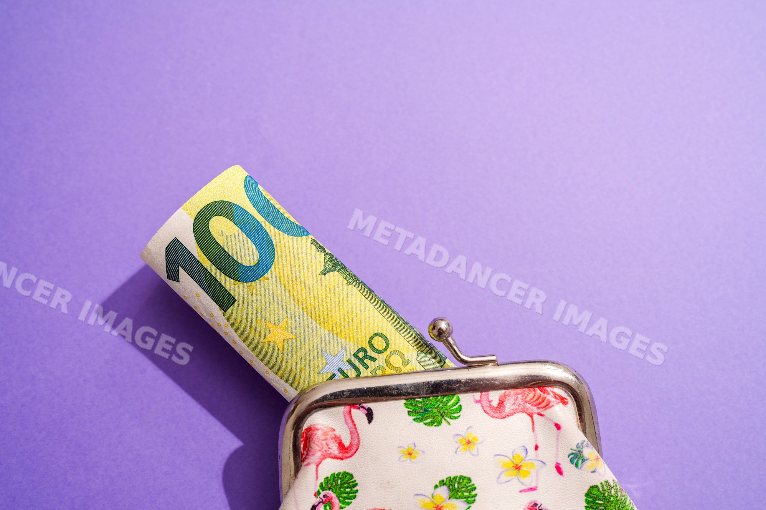 Rolled 100 euro bill in flamingo print coin purse on purple background