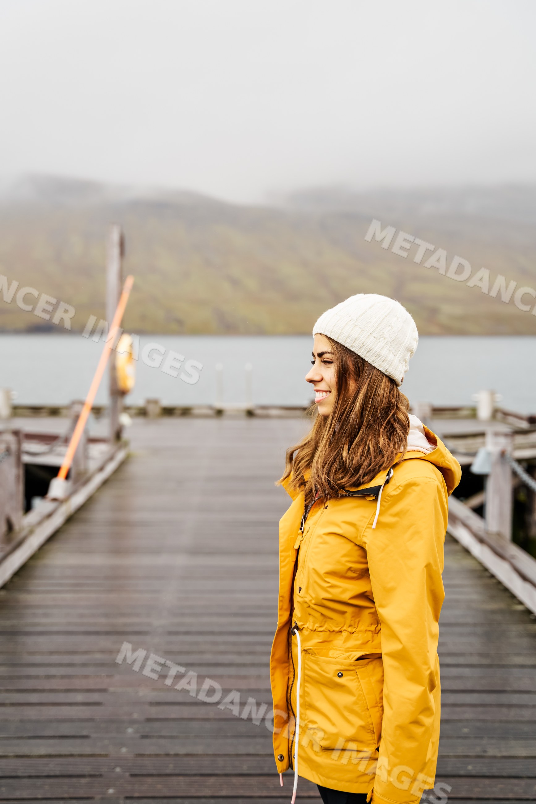 A white woman in yellow jacket smiles on a wooden pier