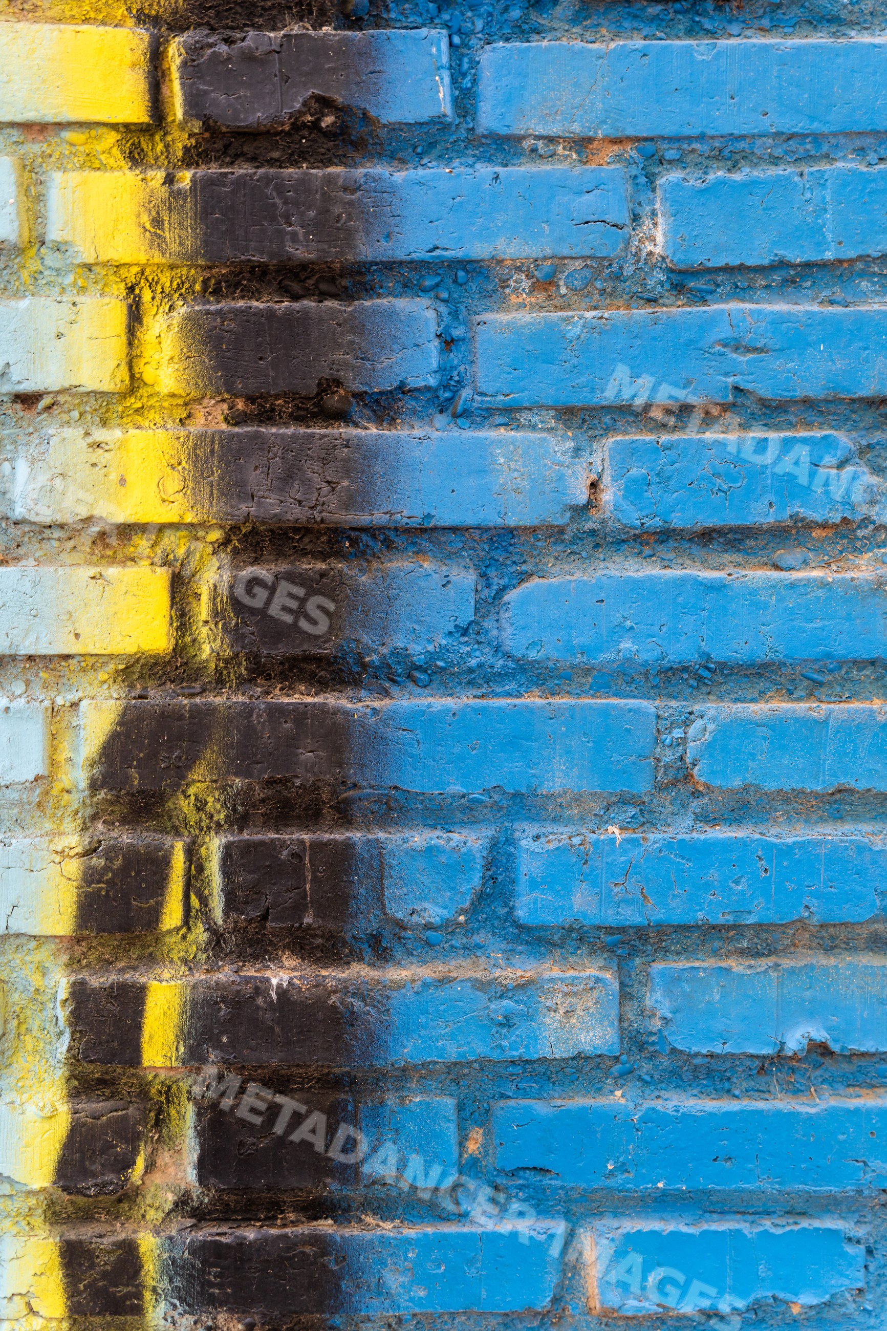 Blue brick wall in Spain with yellow and black weathered paint