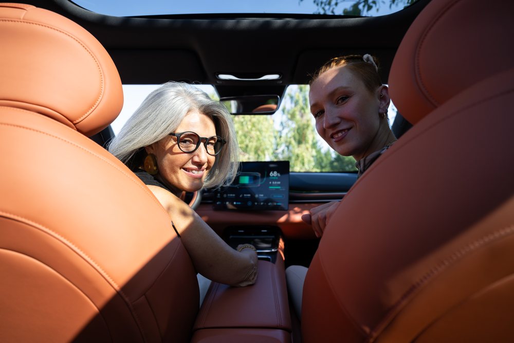 Two white women looking back inside a car with tan leather seats