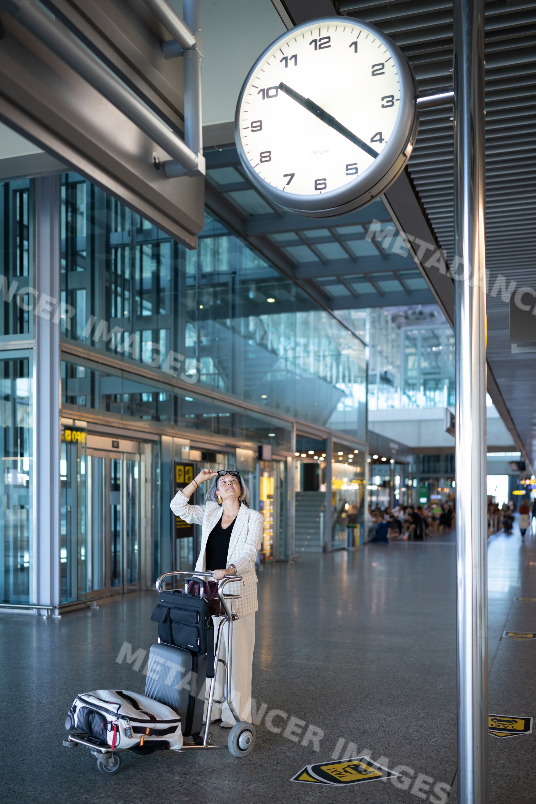 White woman traveler with luggage trolley waiting at airport terminal
