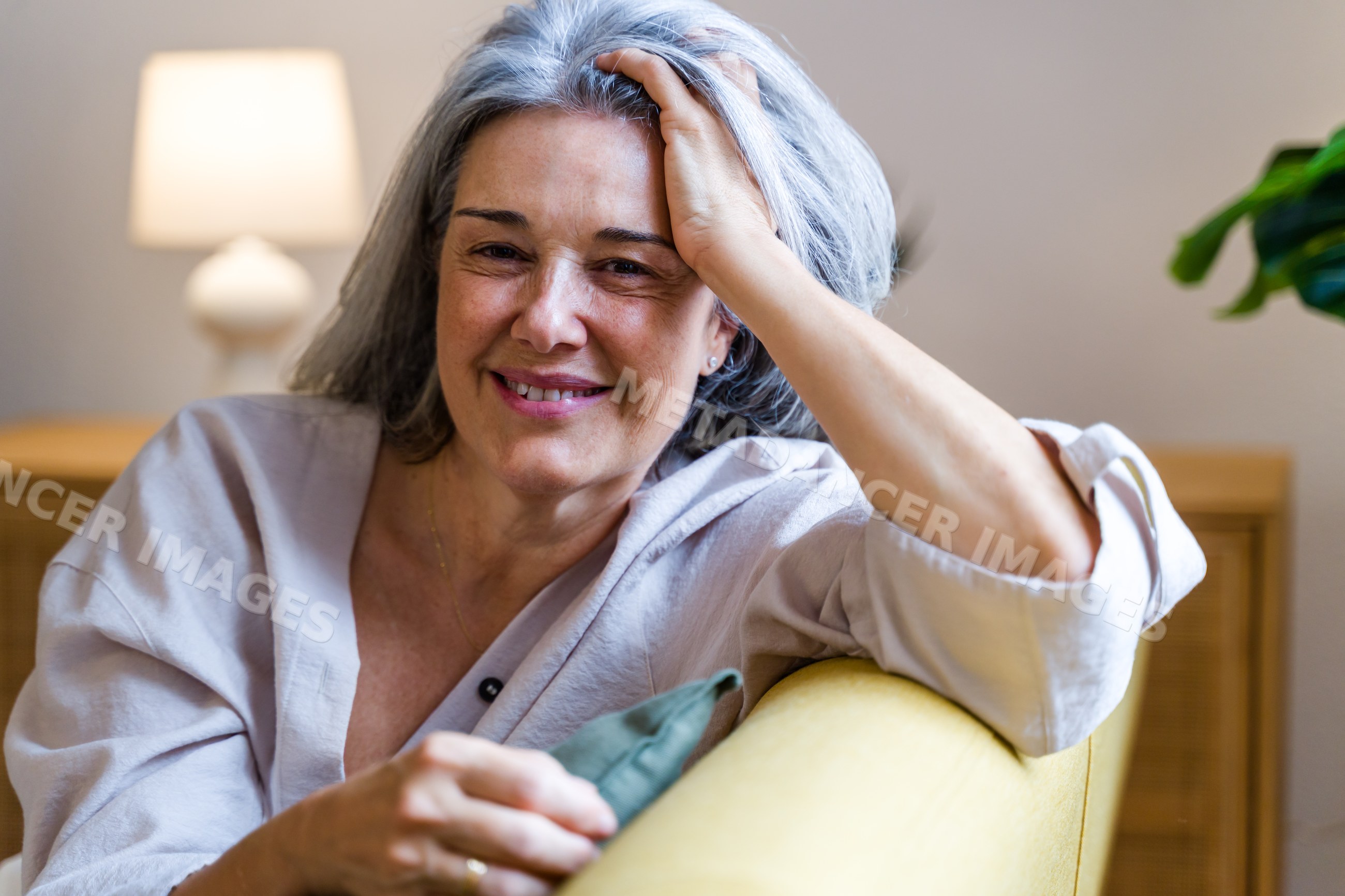 Middle-aged white woman smiling on yellow couch in cozy living room