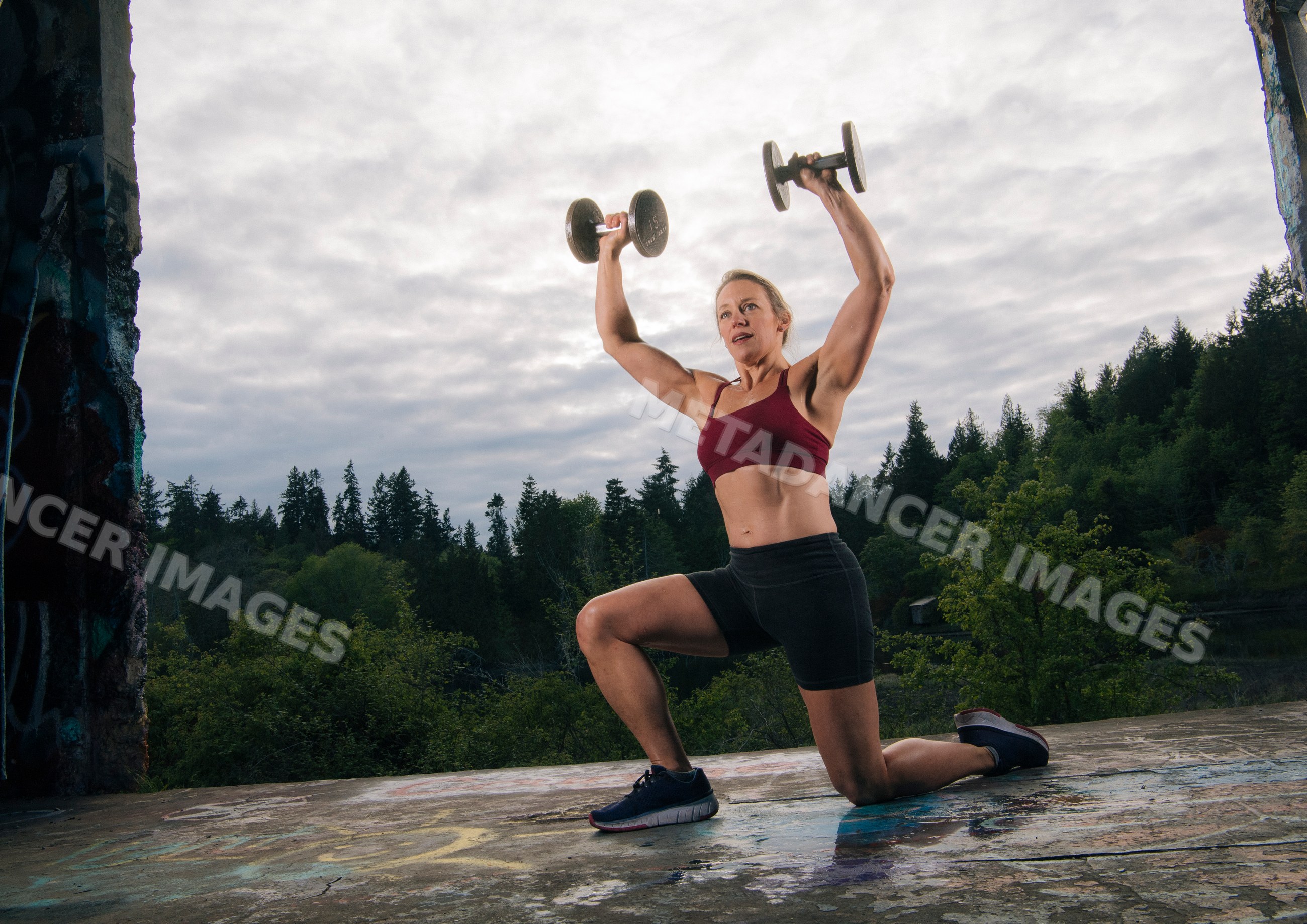 White woman exercising outdoors lifting dumbbells in forest setting