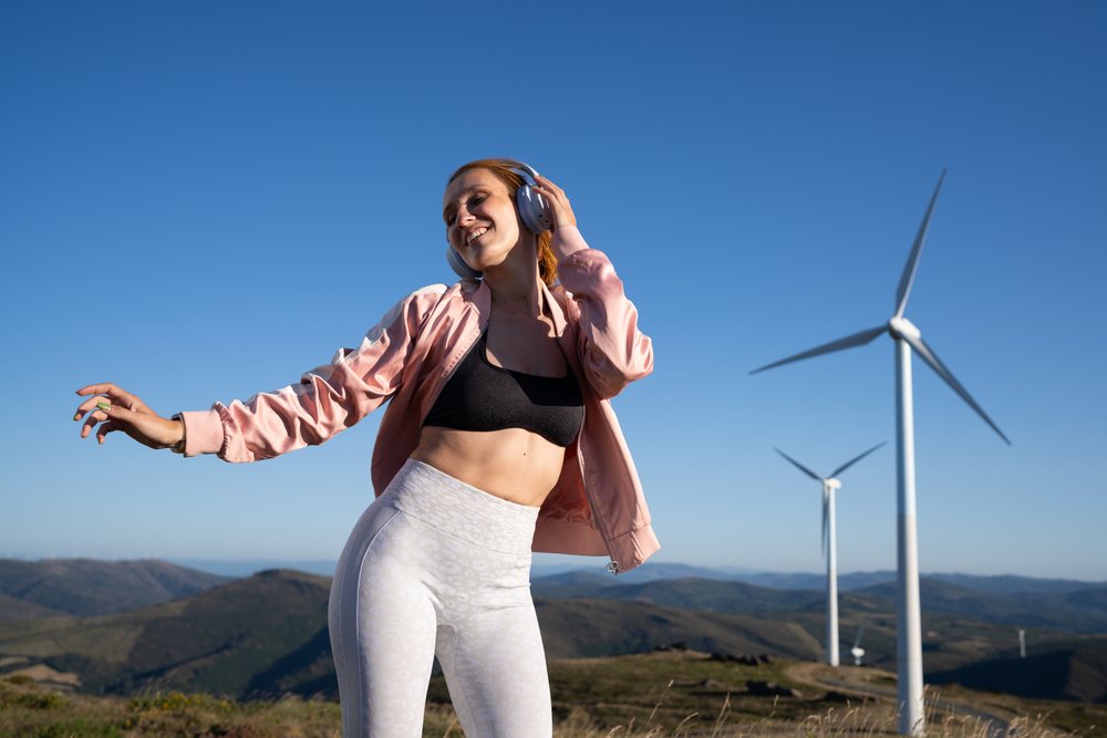 Young white woman dancing near wind turbines in Galicia, Spain