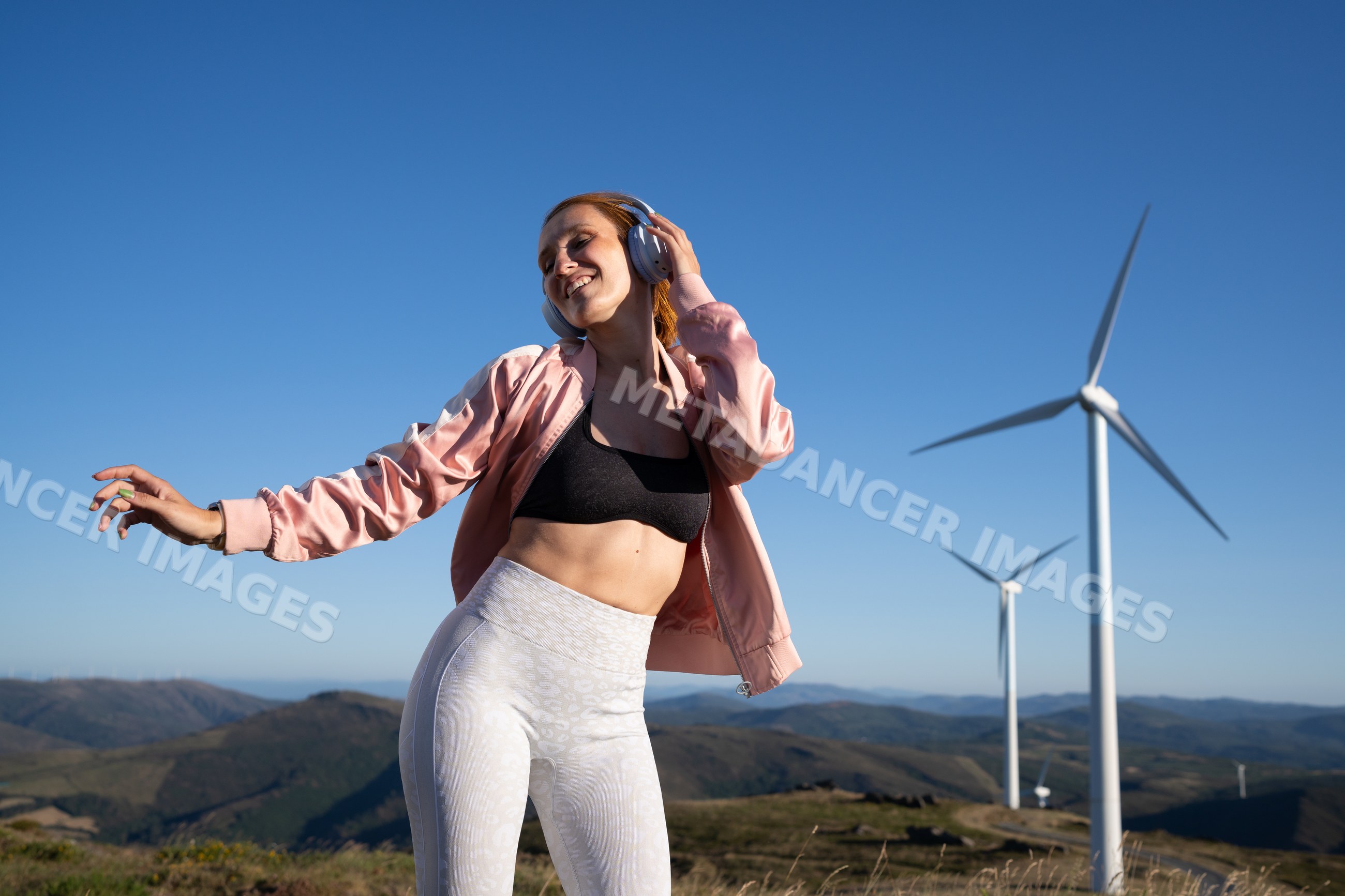 Young white woman dancing near wind turbines in Galicia, Spain