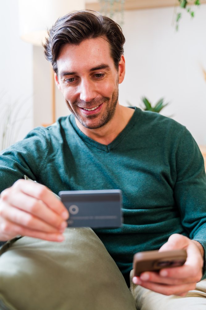 White man using smartphone and credit card for online payment indoors