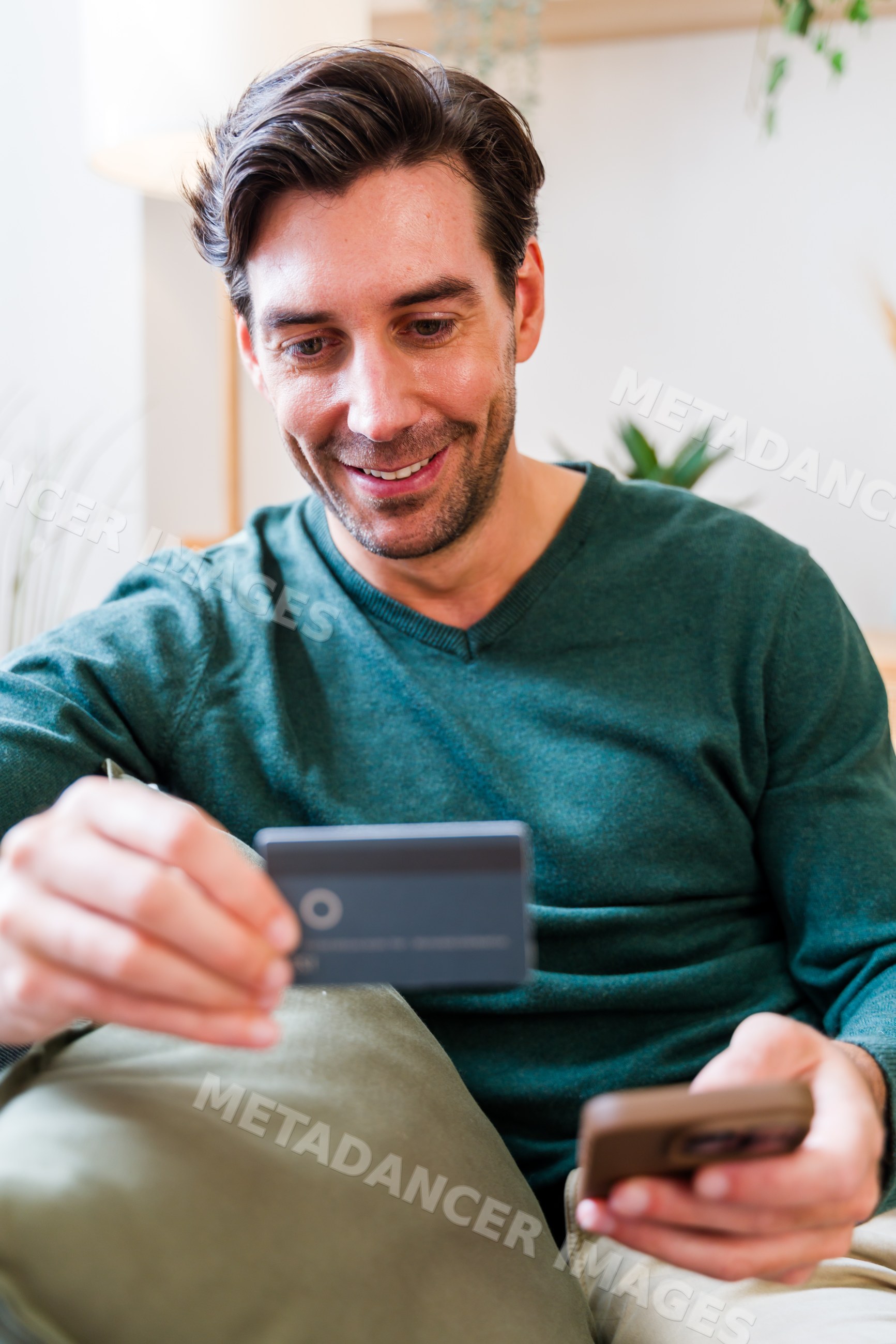 White man using smartphone and credit card for online payment indoors