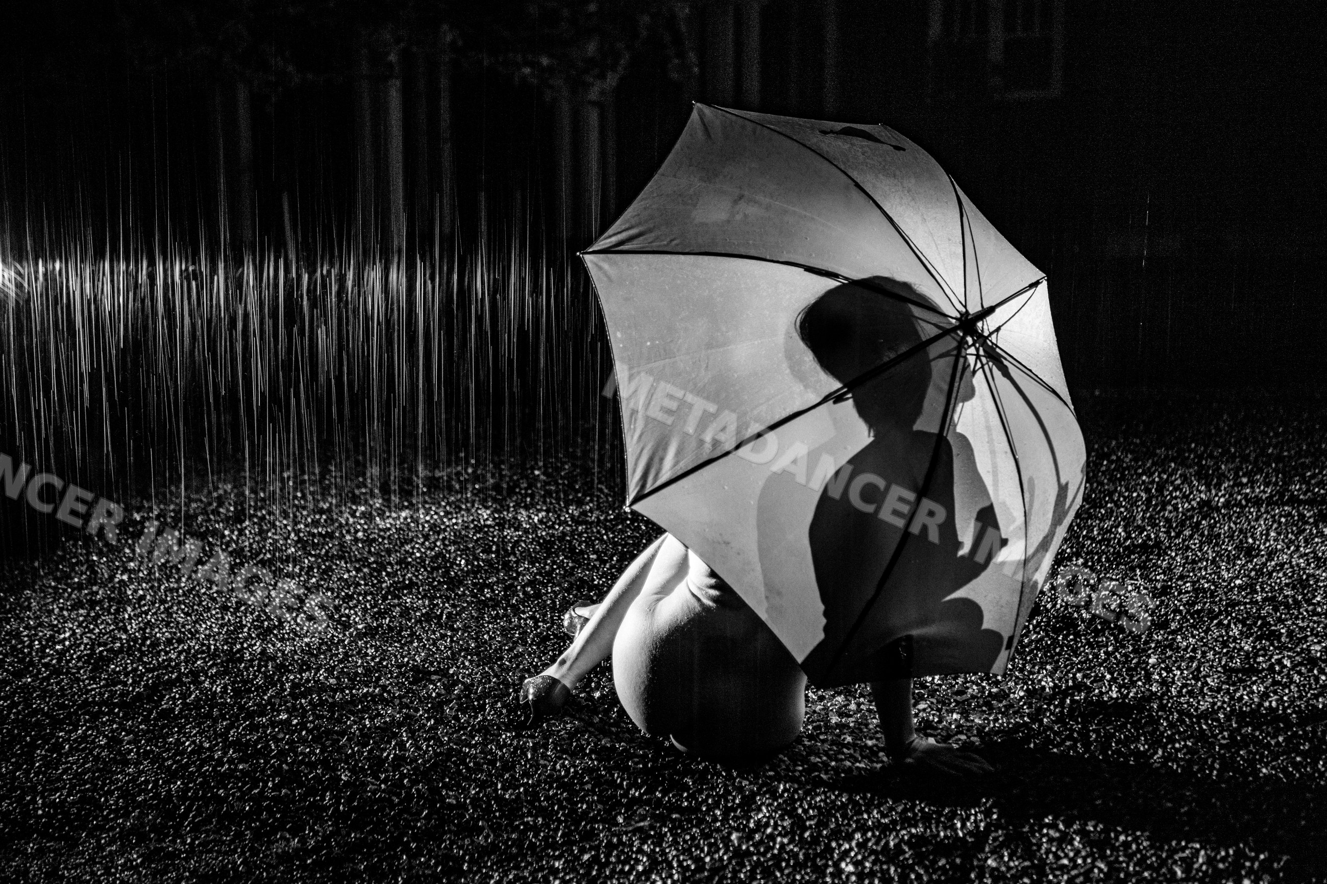 Nude white person sitting under umbrella in the rain at night