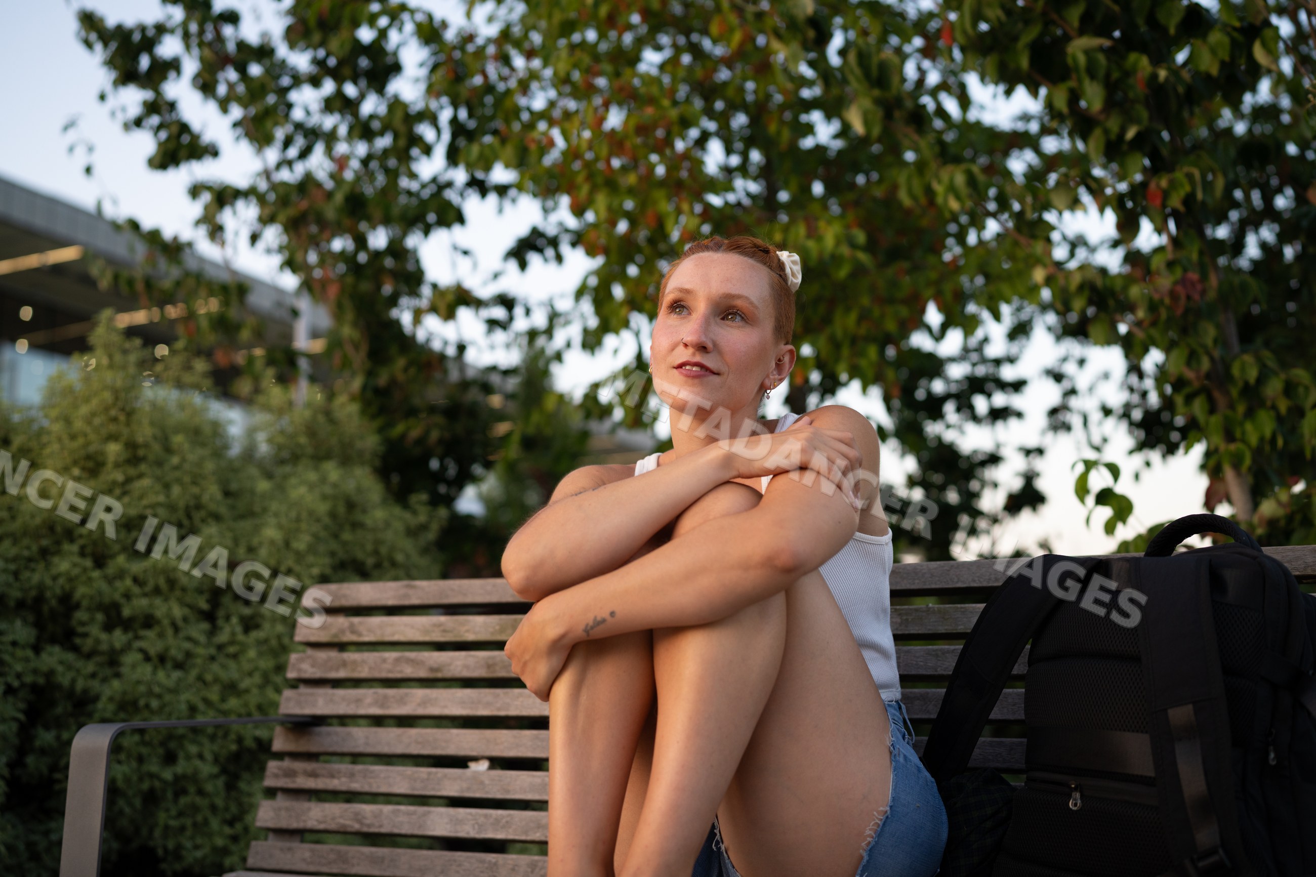 A young white woman sitting on a bench outdoors