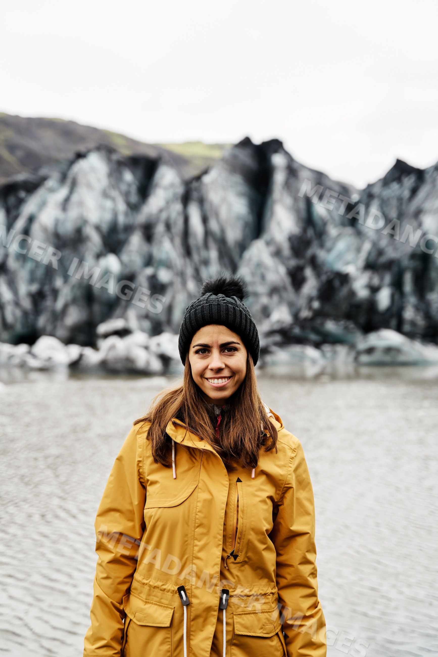 A white woman in warm clothes standing by a glacier lake