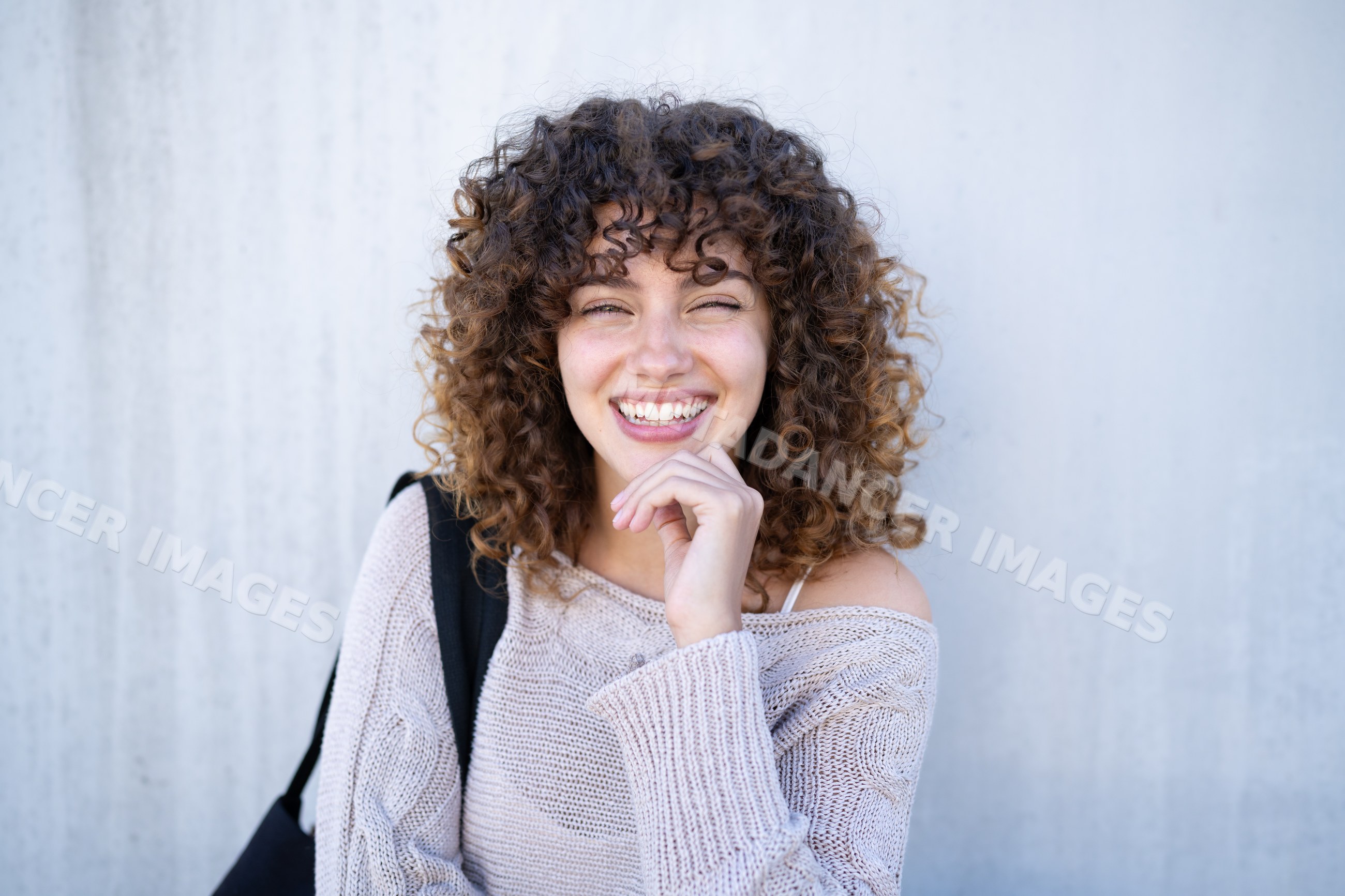 Young white woman with curly hair smiling outdoors in beige sweater