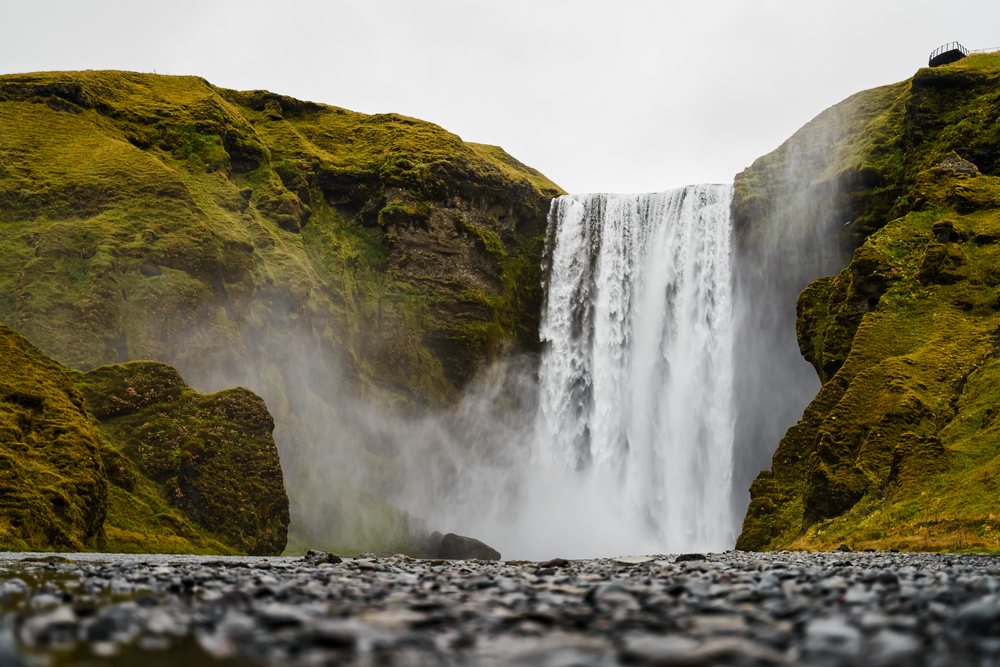 Waterfall flows over mossy cliffs creating mist