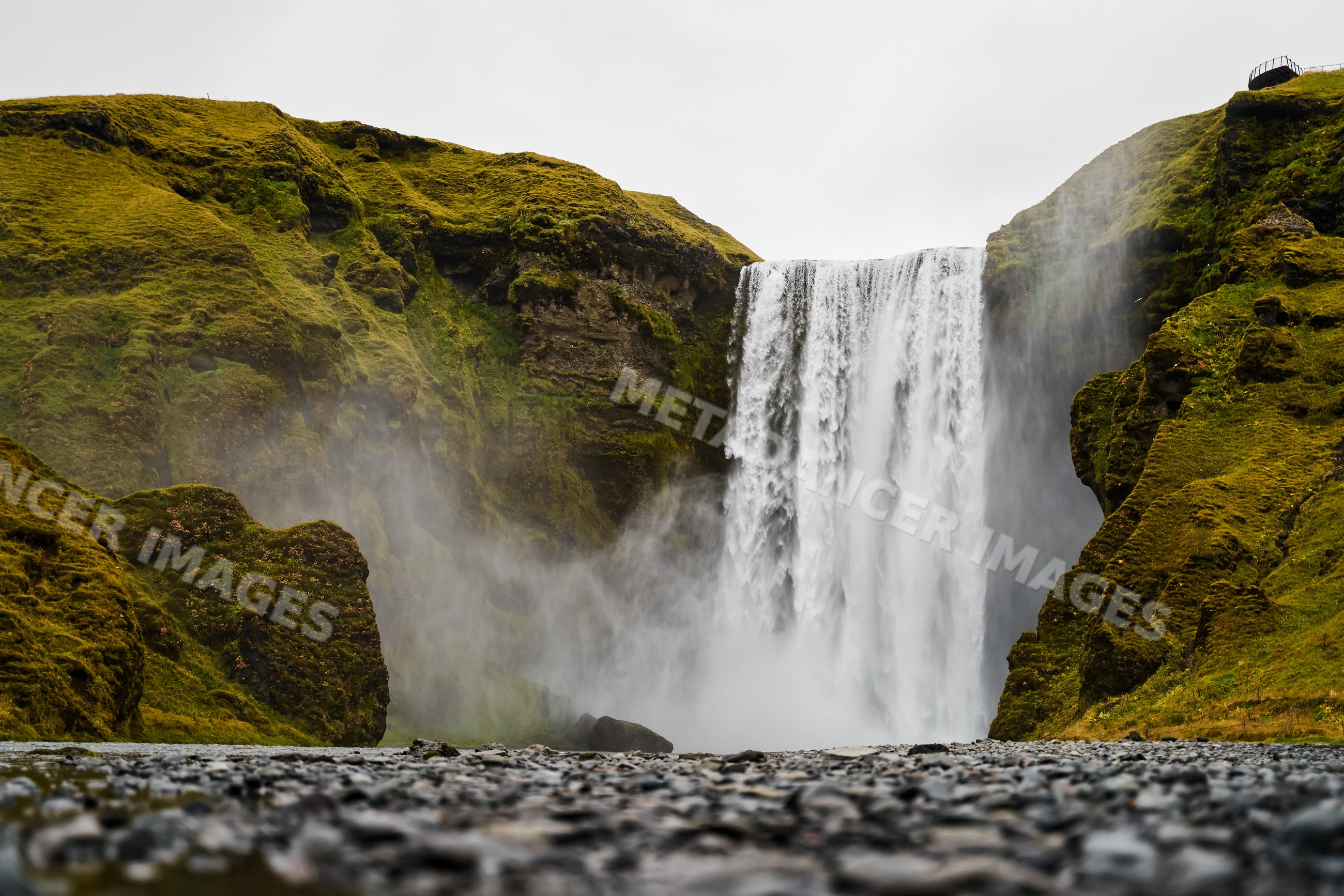 Waterfall flows over mossy cliffs creating mist