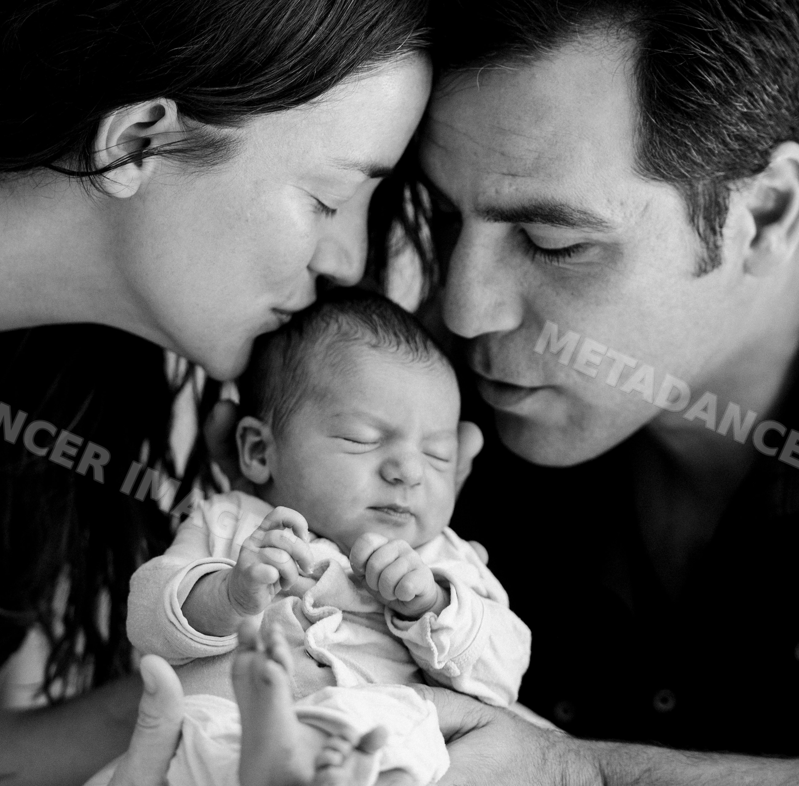 Newborn baby held and kissed by loving parents